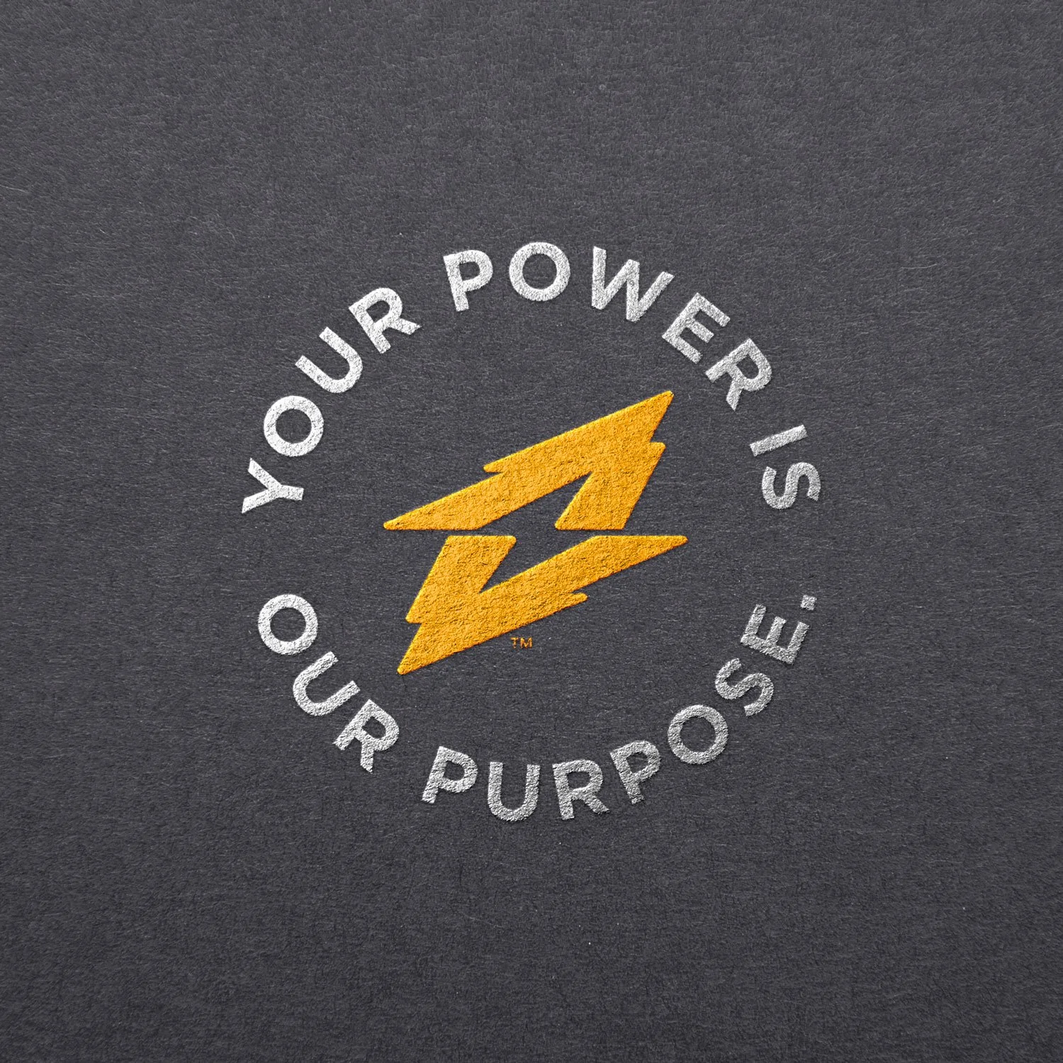 Embossed Action Battery logo emblem on black paper. Emblem reads “Your power is our purpose”.