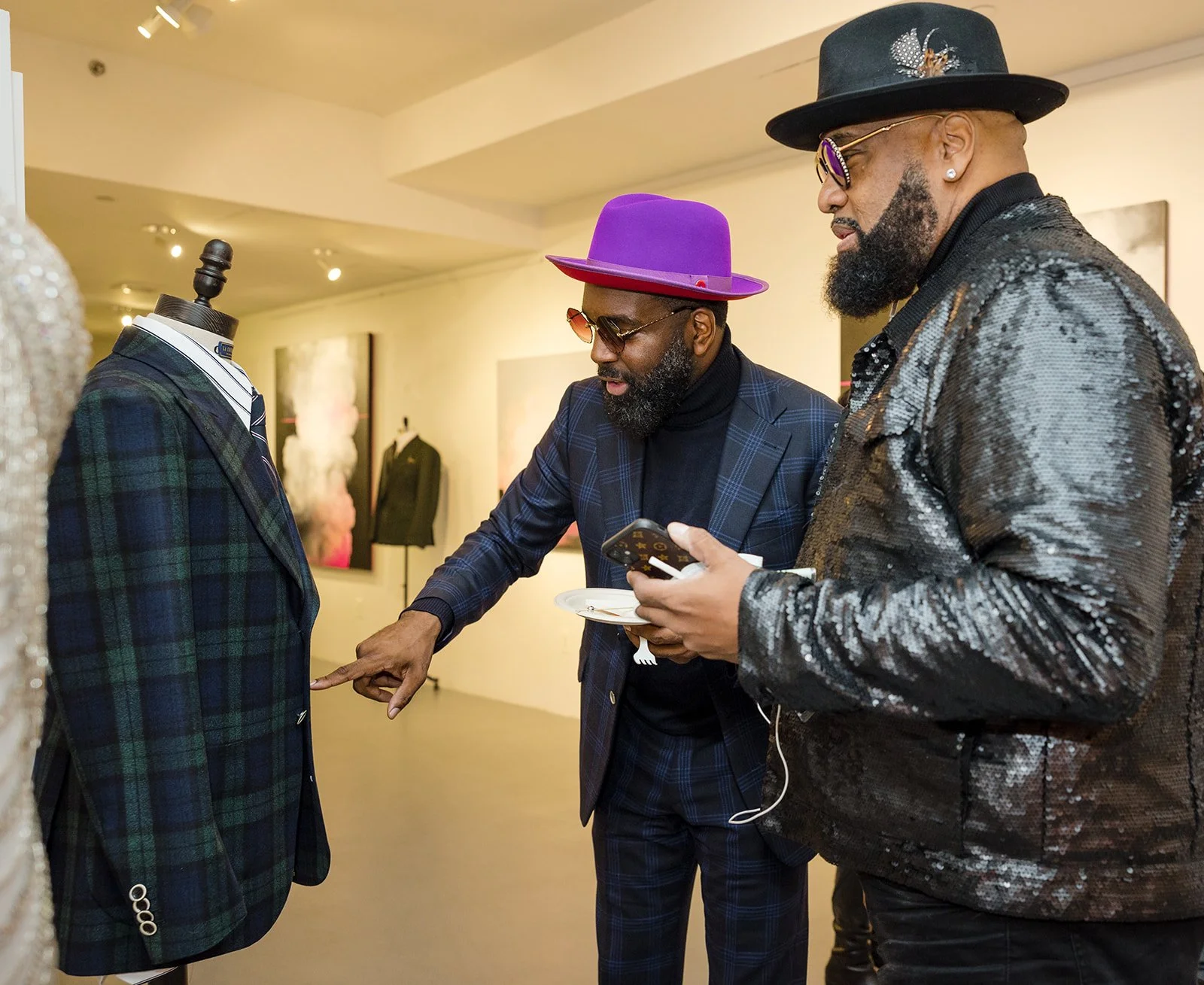 Two men dressed fashionably in an art gallery, looking at a suit on display and examining it closely.