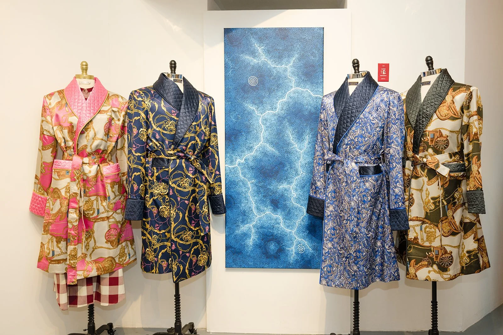 Four mannequins dressed in colorful patterned robes and pajamas, standing in front of a blue lightning artwork.