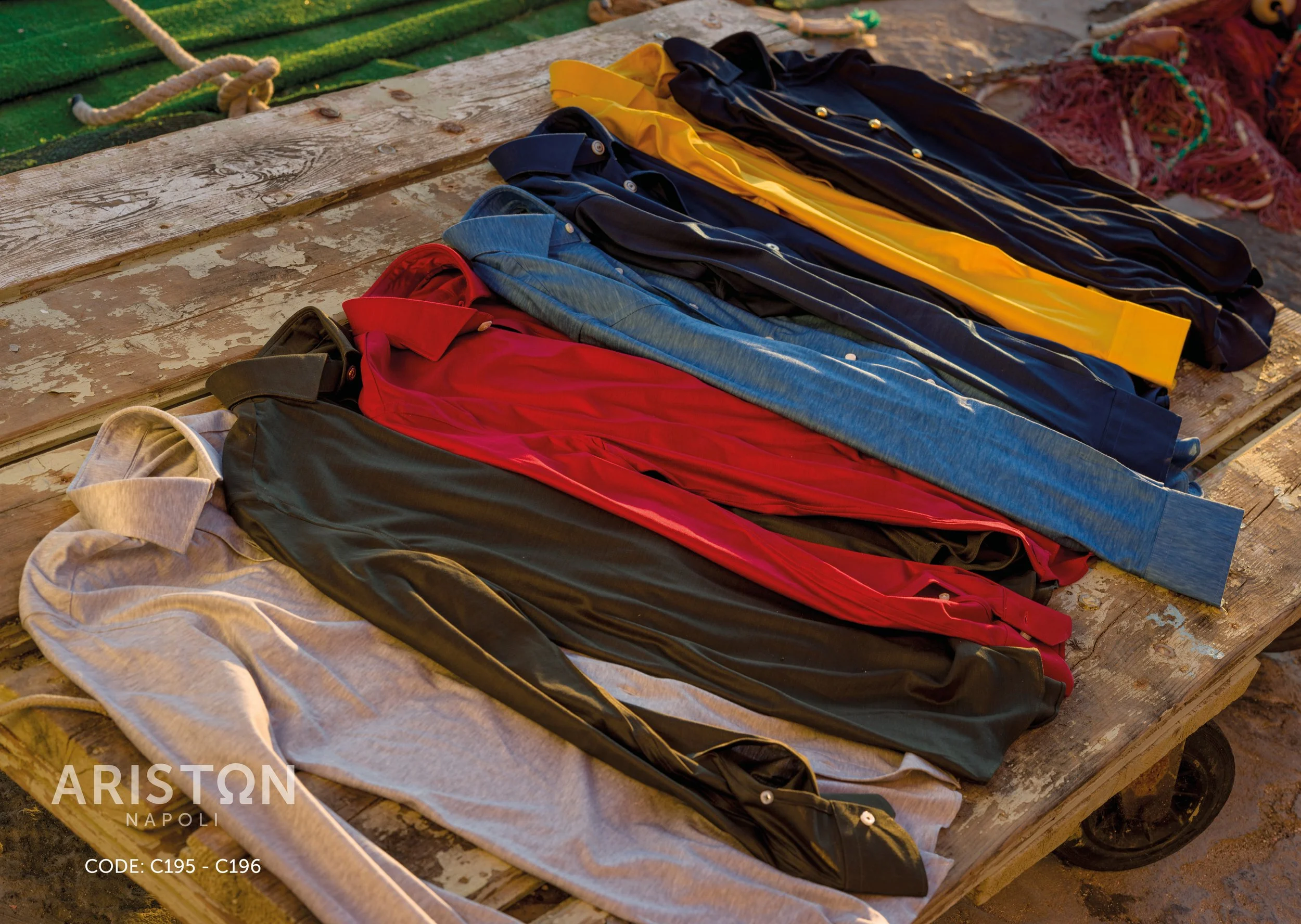Five colorful pairs of pants laid out on a wooden surface, with the text 'Ariston Napoli' and codes in the bottom left corner.