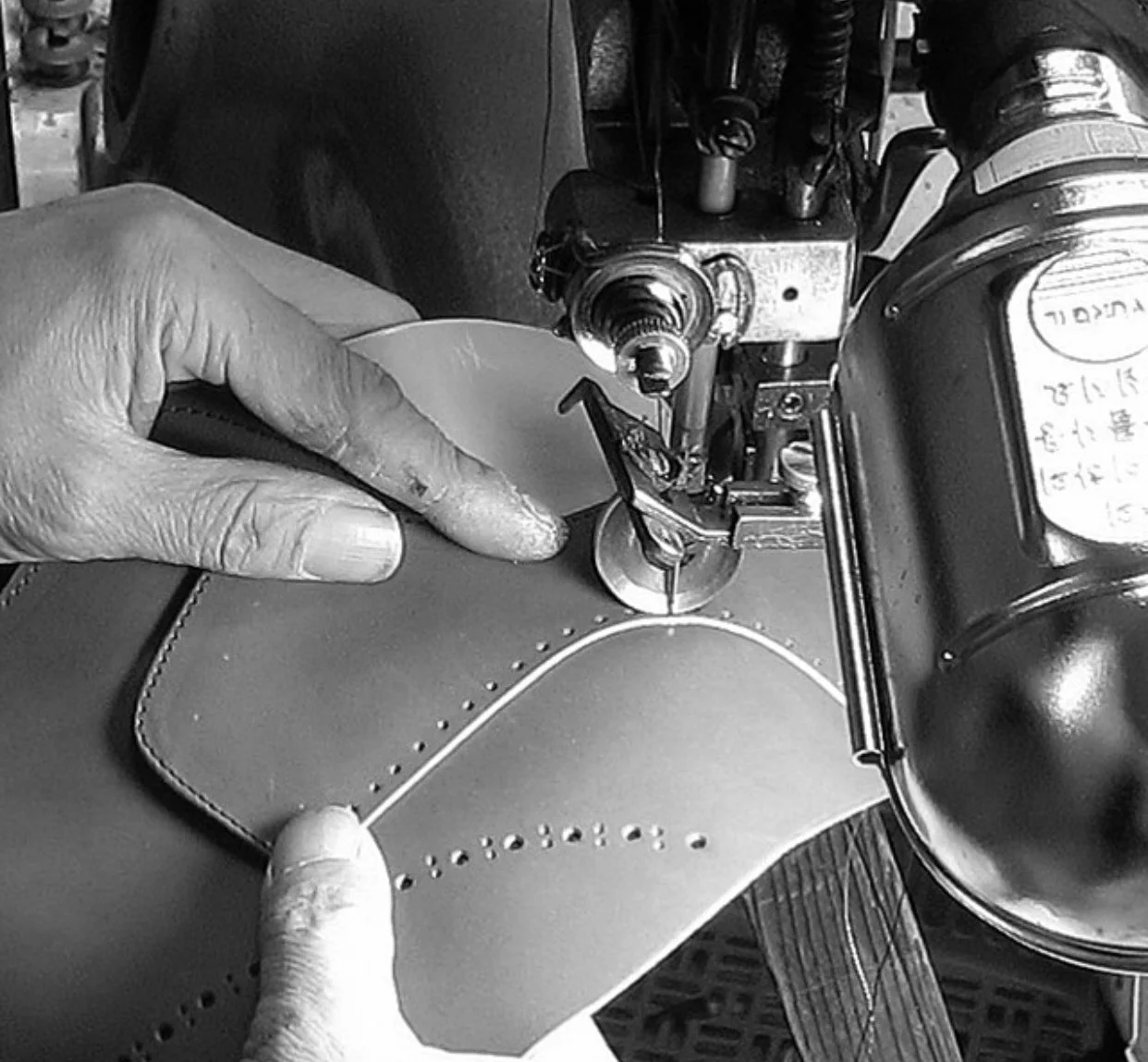 A person sewing perforations in leather on a sewing machine.