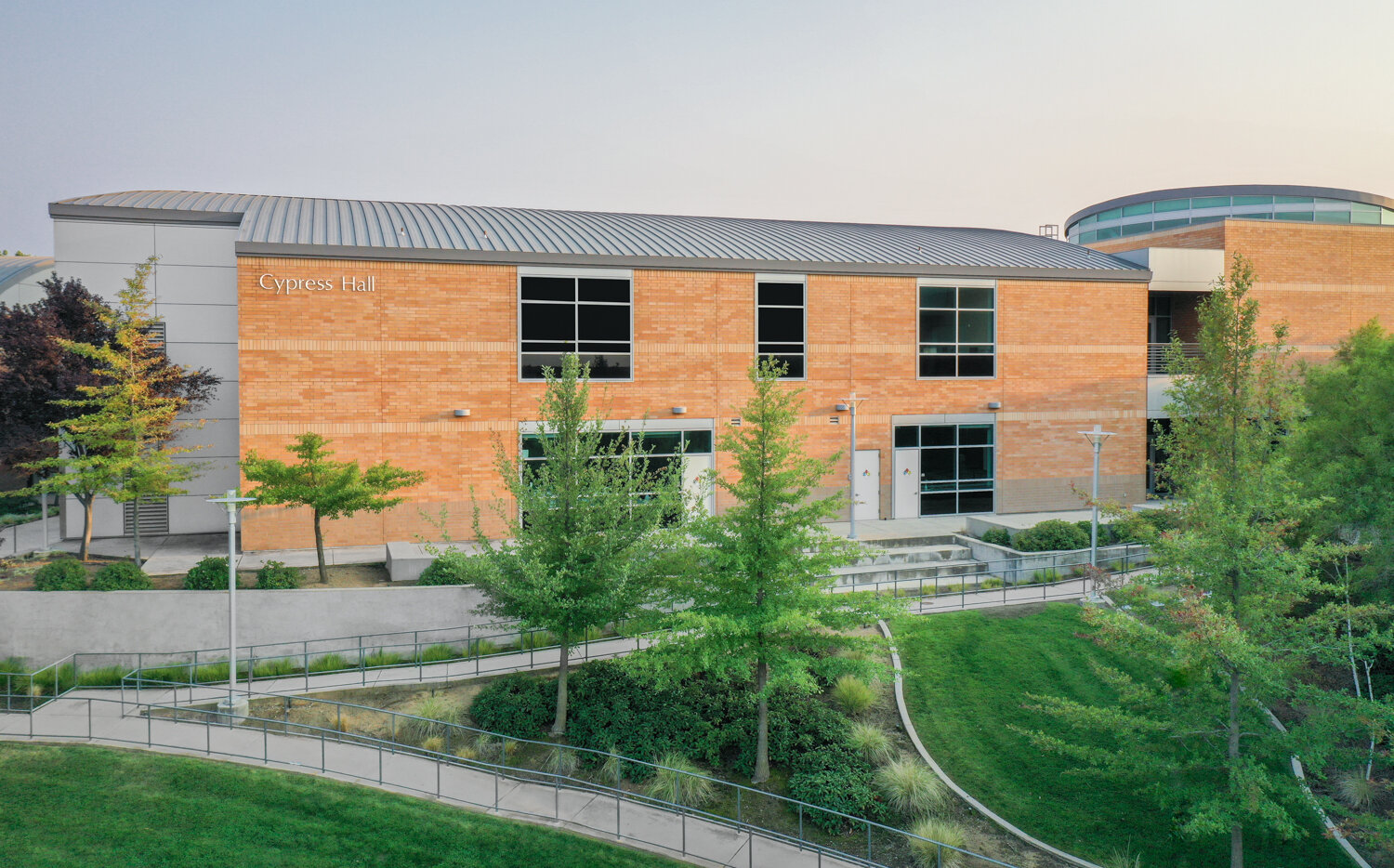 Exterior view of Cypress Hall at Folsom Lake College, a brick campus building with large windows, surrounded by green trees and landscaped walkways.