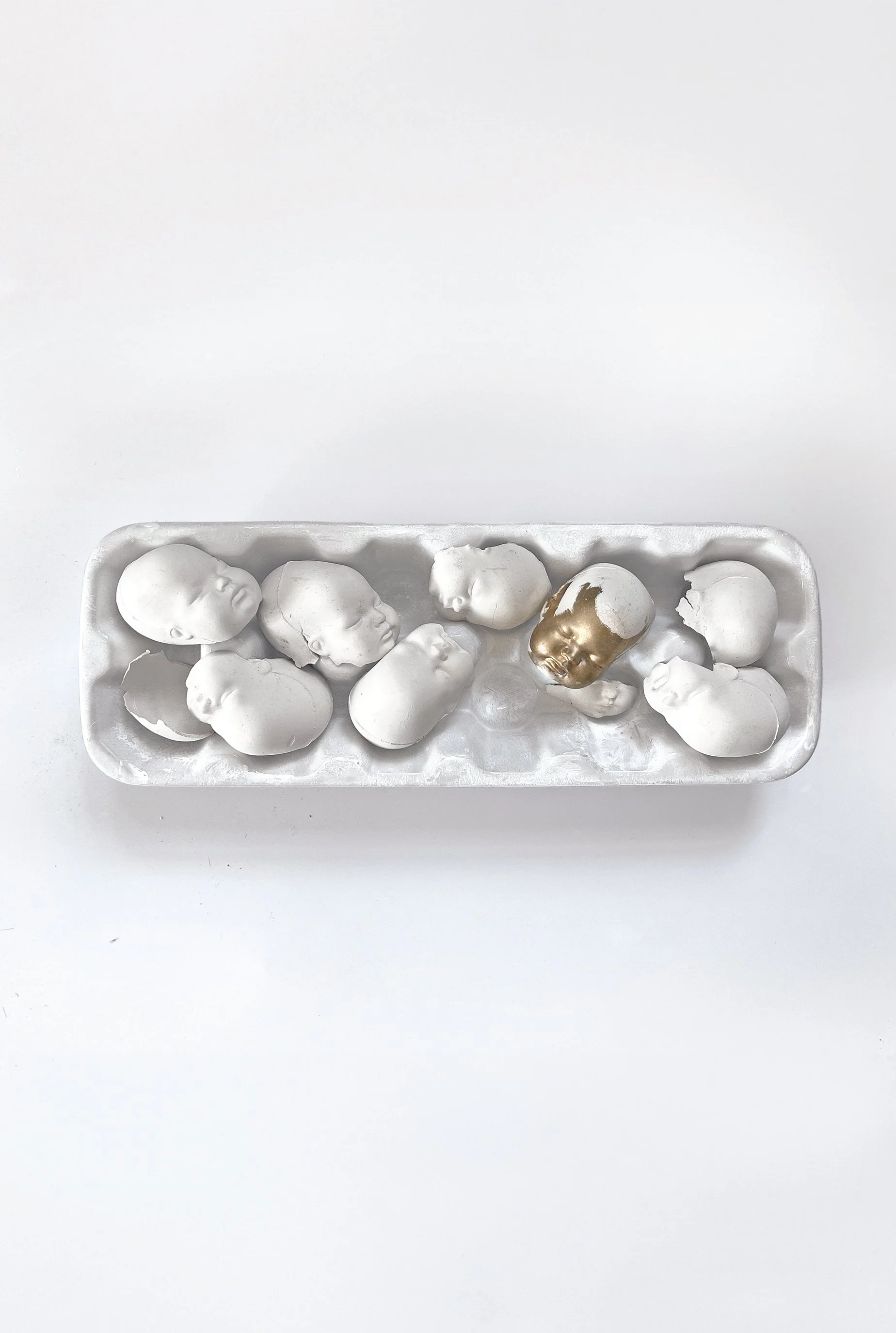 Eggshells in an open carton, with one gold-painted eggshell among them.