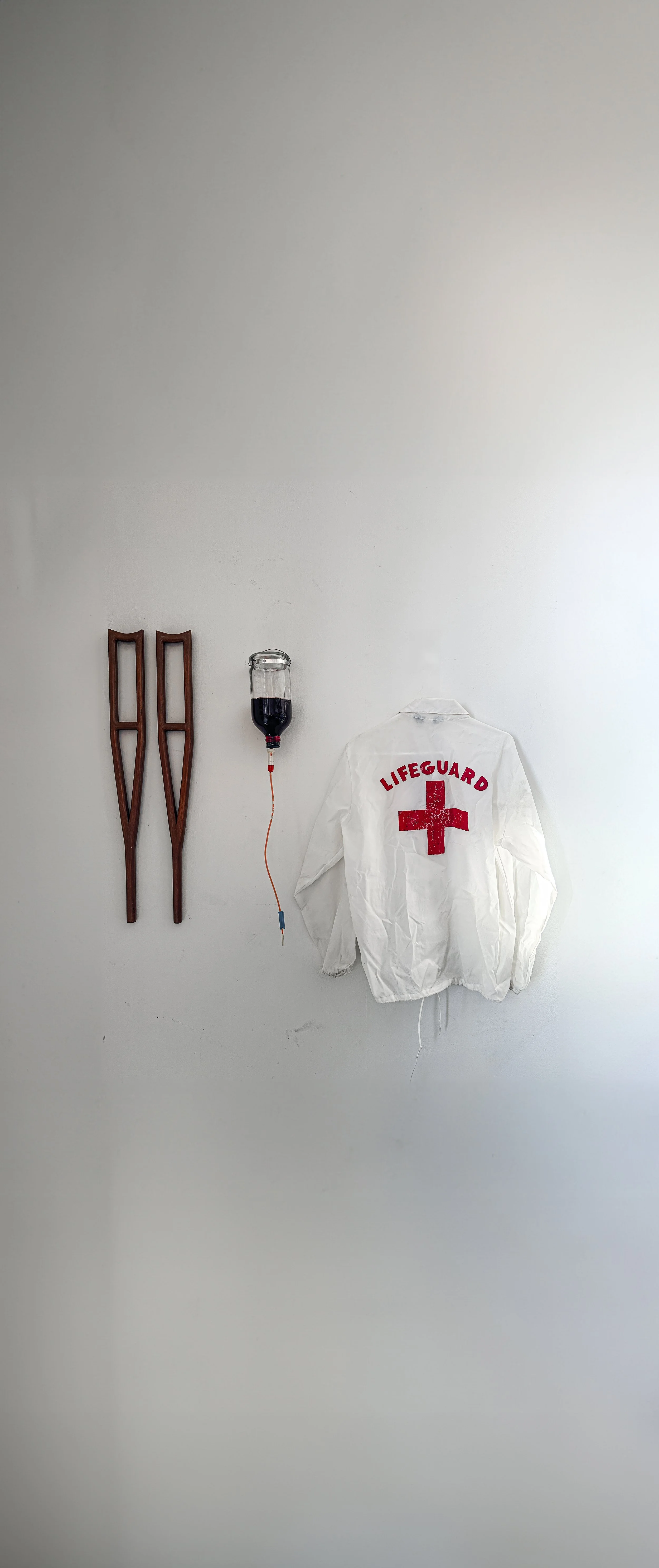 Wall with wooden snowshoes, a medical IV bag, and a white lifeguard jacket with a red cross.