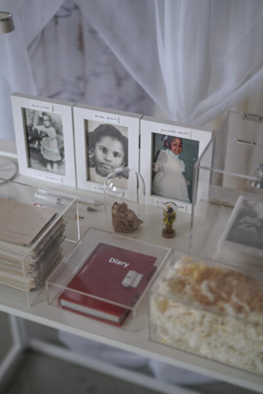 A display of black-and-white and color photographs of children, a diary, small rocks, and decorative items on a table.