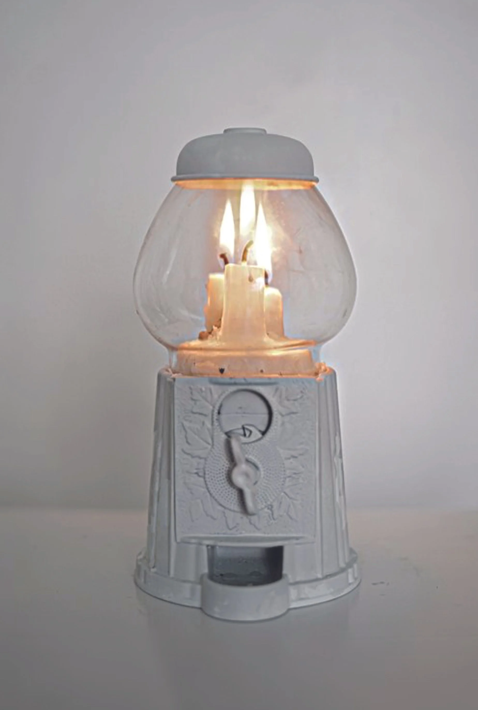 A vintage white lantern with a small flame inside, sitting on a white surface against a plain background.