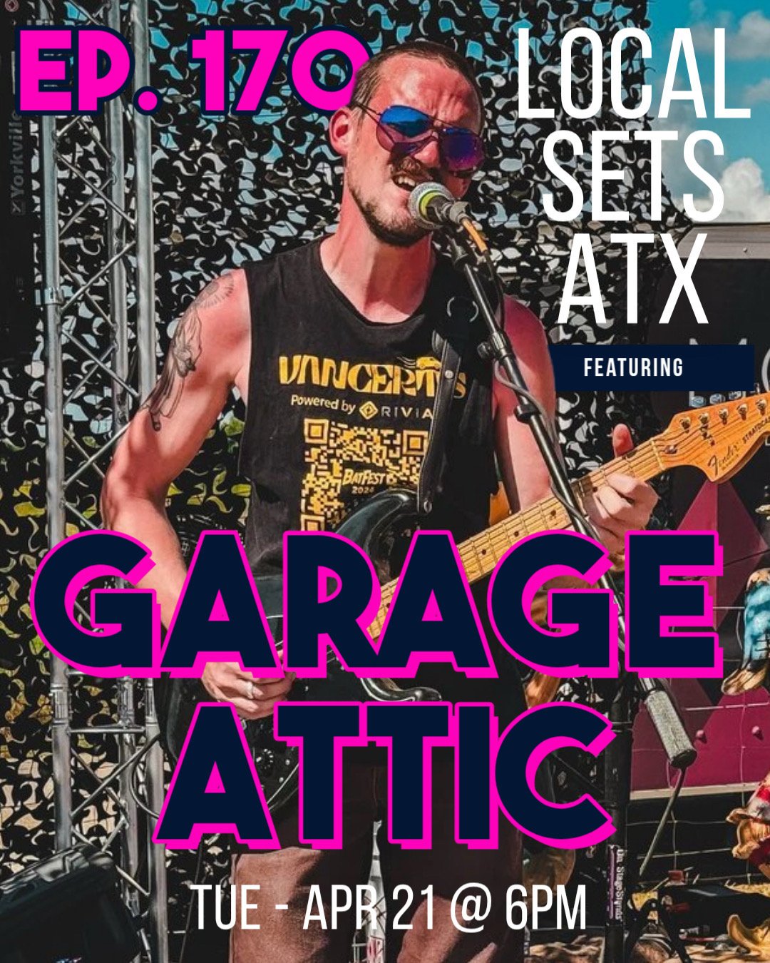 A male musician with tattoos on his arm, wearing sunglasses and a sleeveless black shirt, is playing an electric guitar and singing into a microphone on a stage.