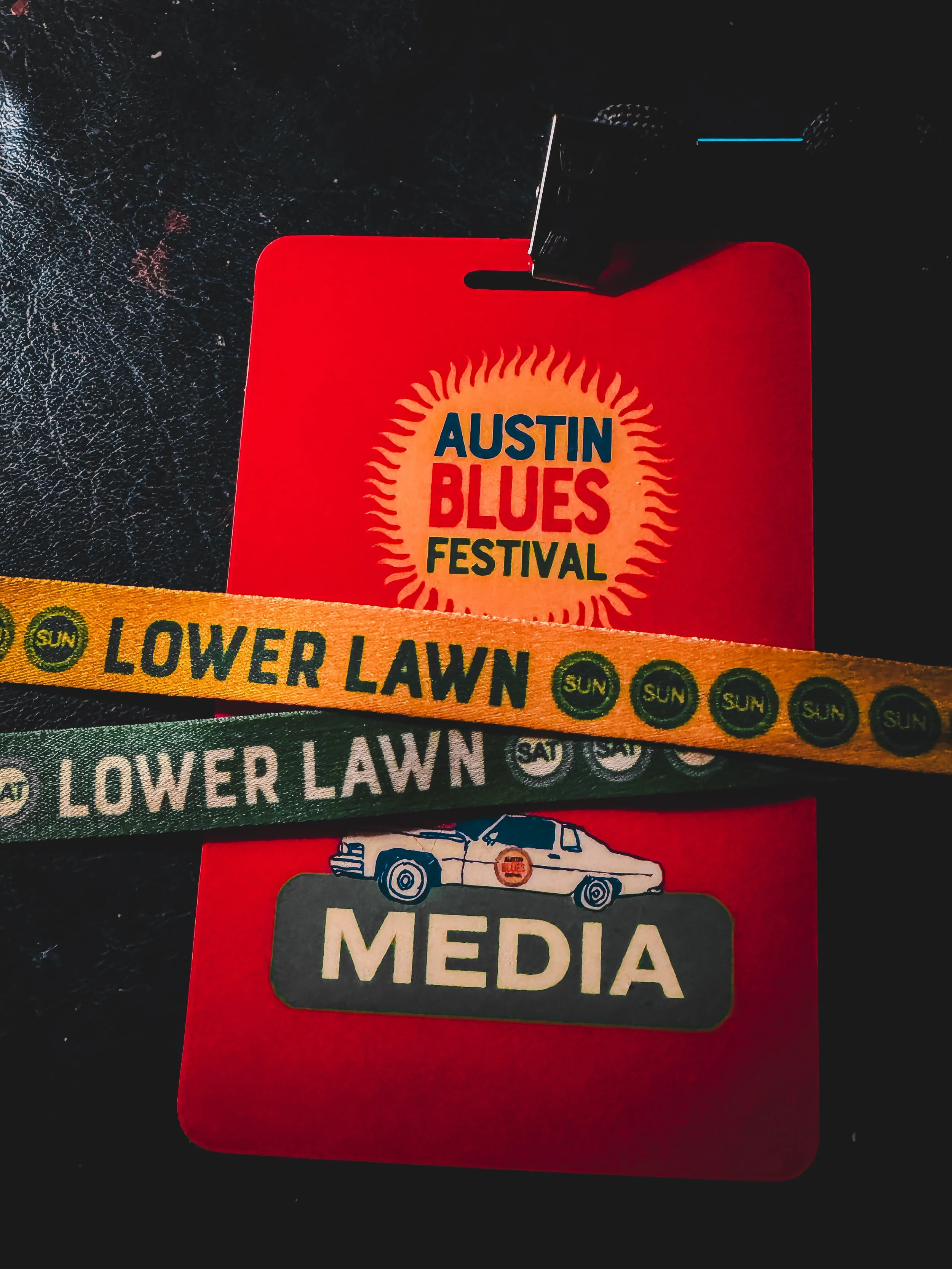 Close-up of event passes and wristbands for the Austin Blues Festival, with a portion of a 'Lower Lawn' wristband and a media pass visible.