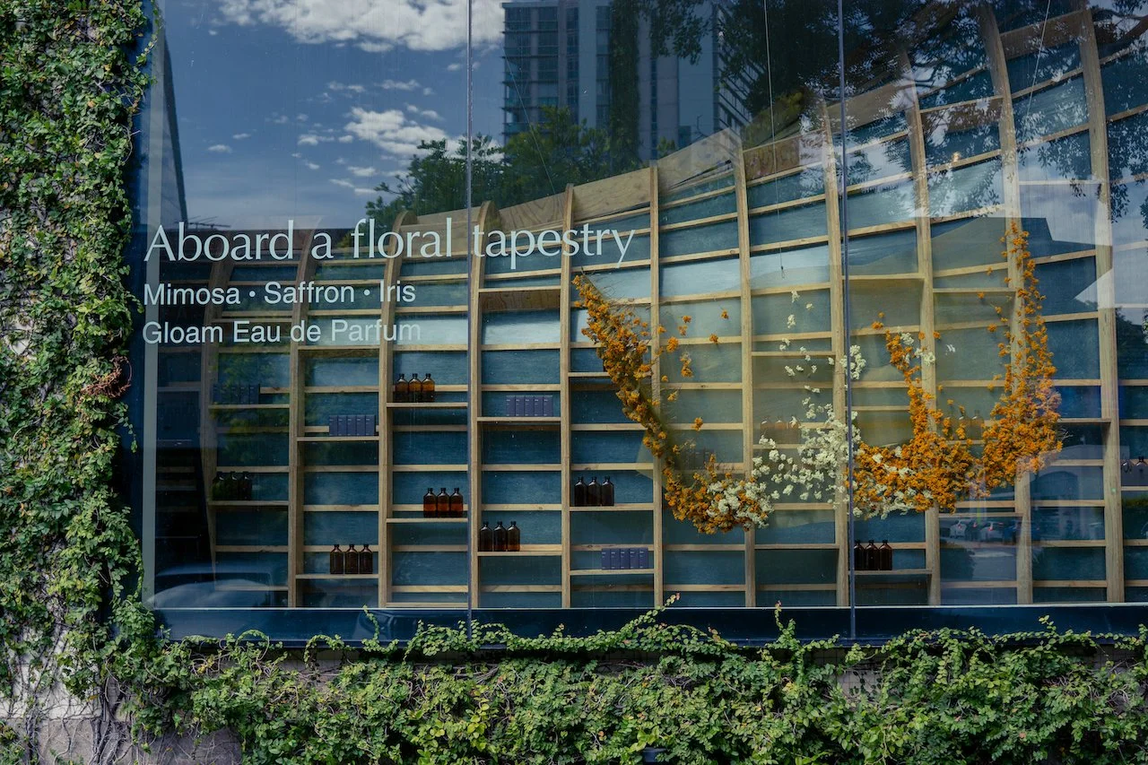 Aesop James Street Storefront. An installation by BRAER for the release of Gloam parfum. Ari Messina captured images detailing the floral installation, a large mesh of golden flowers hangs in the window of the leafy street. 