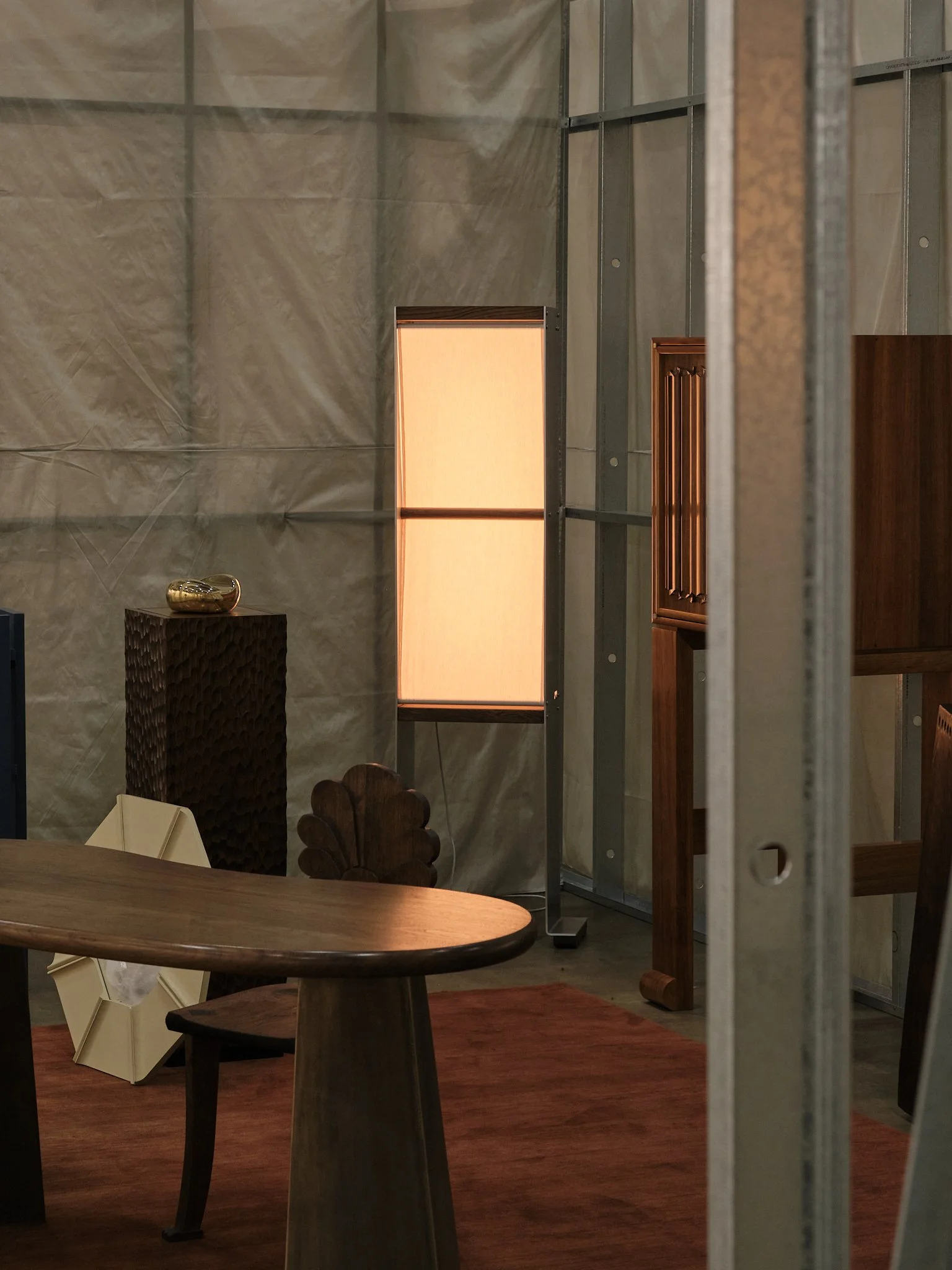 Interior of a furniture or decor store with various wooden tables and chairs, a tall standing lamp with a rectangular shade, a decorative vase, and partially visible shelves and frames.