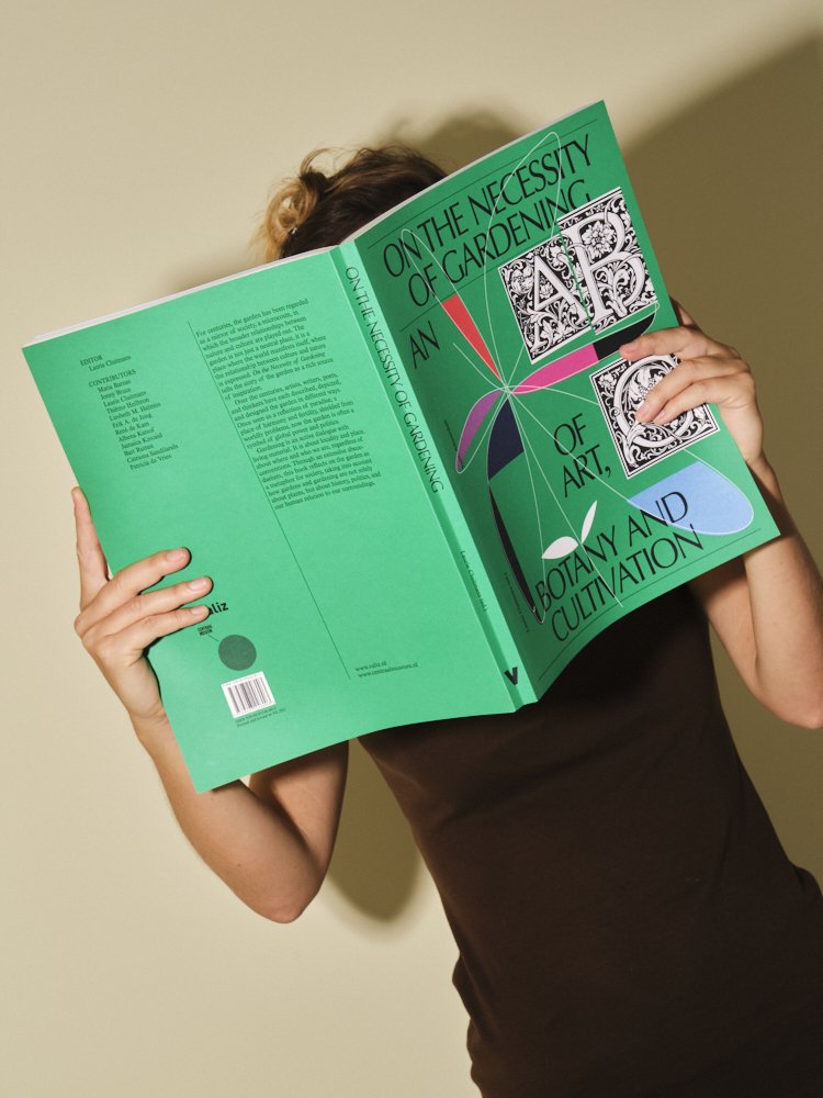 Person holding a book titled "On the Necessity of Gardening: An Exploration of Art, Botany, and Cultivation" in front of their face, with a beige background.
