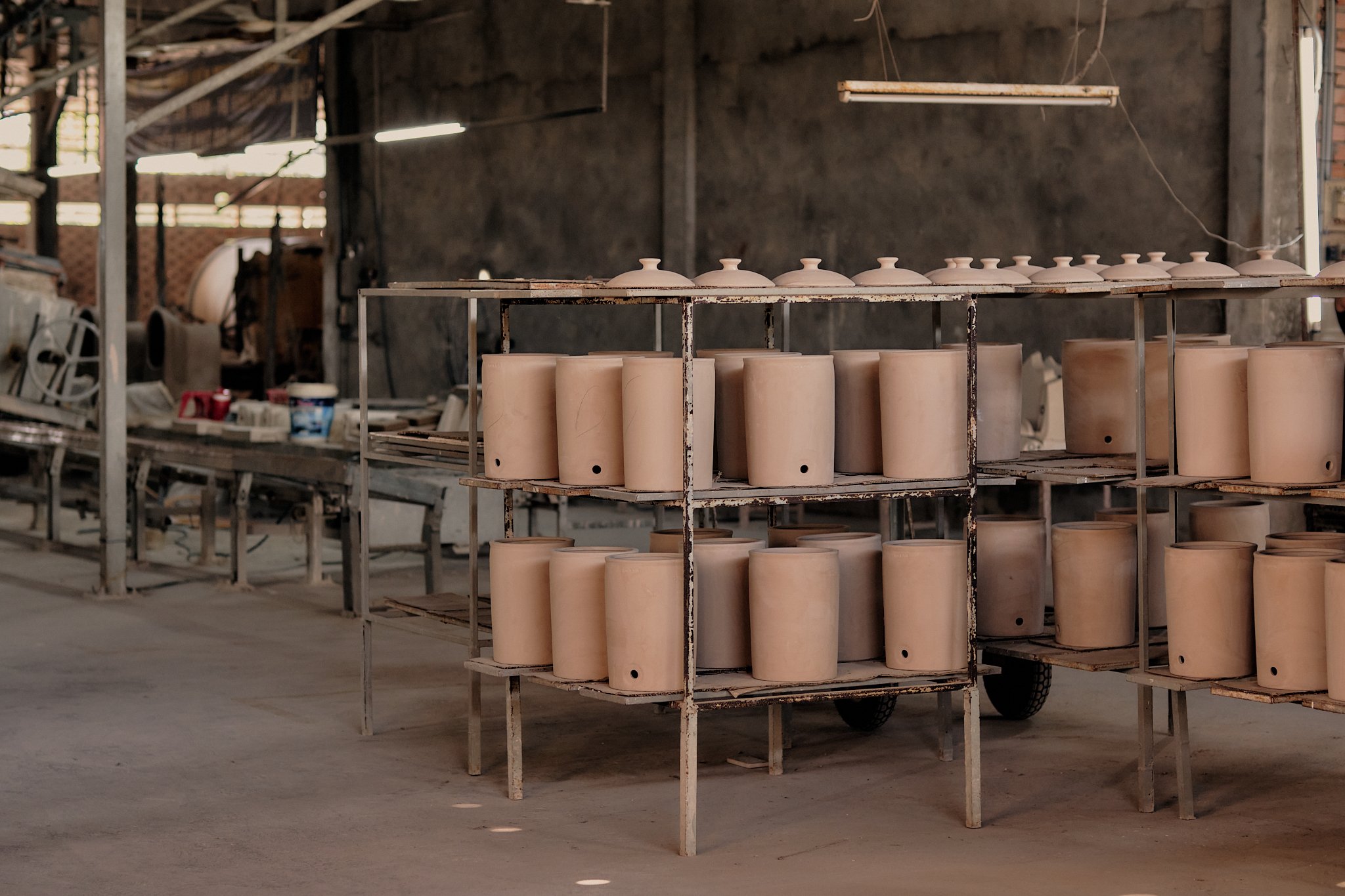 Rows of unglazed ceramic pots on shelving units inside a pottery workshop