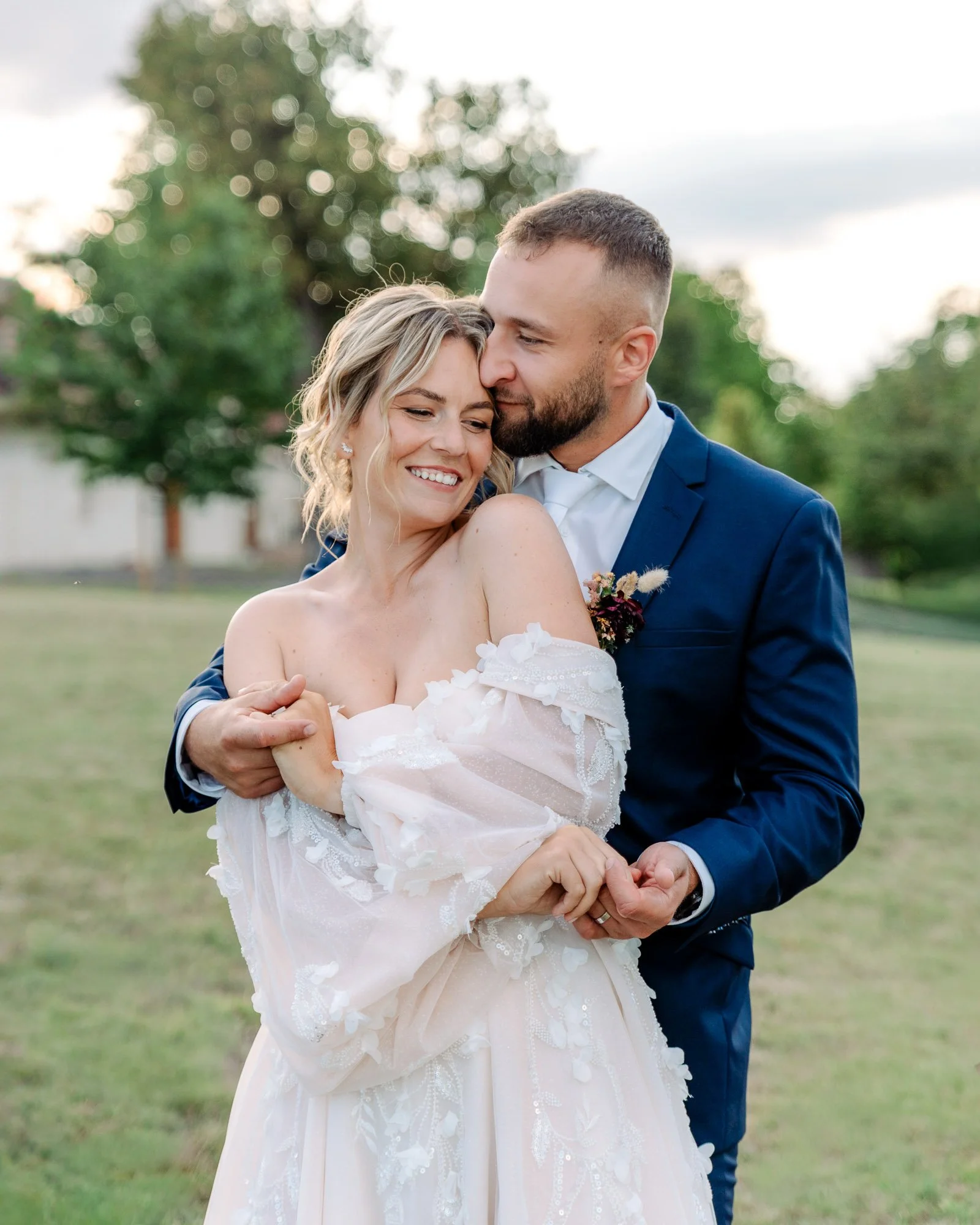 Nevěsta a ženich v přirozeném objetí při svatebním focení v podvečerním světle.