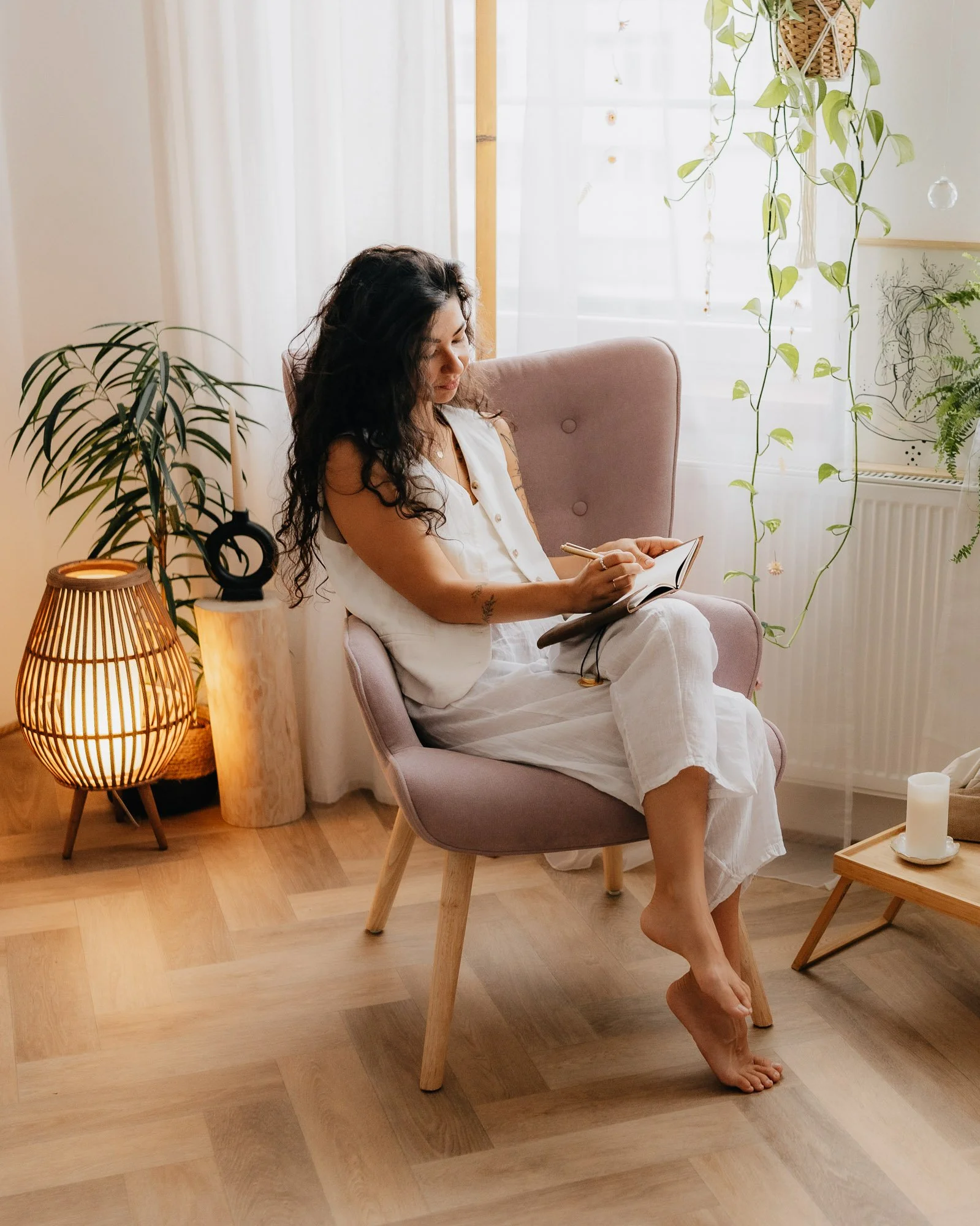 Žena při brandovém focení sedí v křesle u okna a zapisuje si poznámky v přirozeně prosvětleném interiéru.