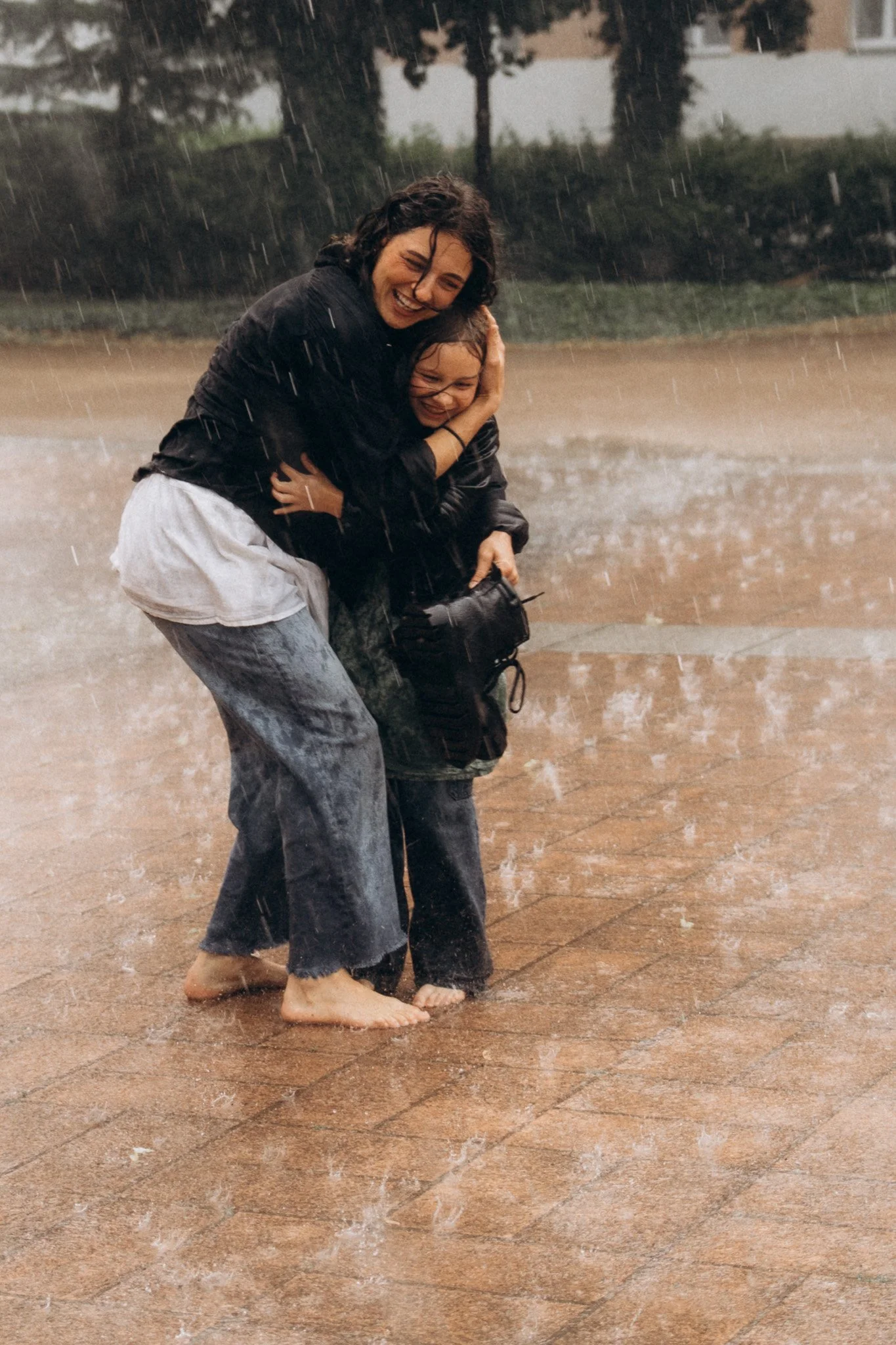 Maminka s dcerou se smějí a objímají během rodinného focení v dešti, přirozená radost a spontánní okamžik venku