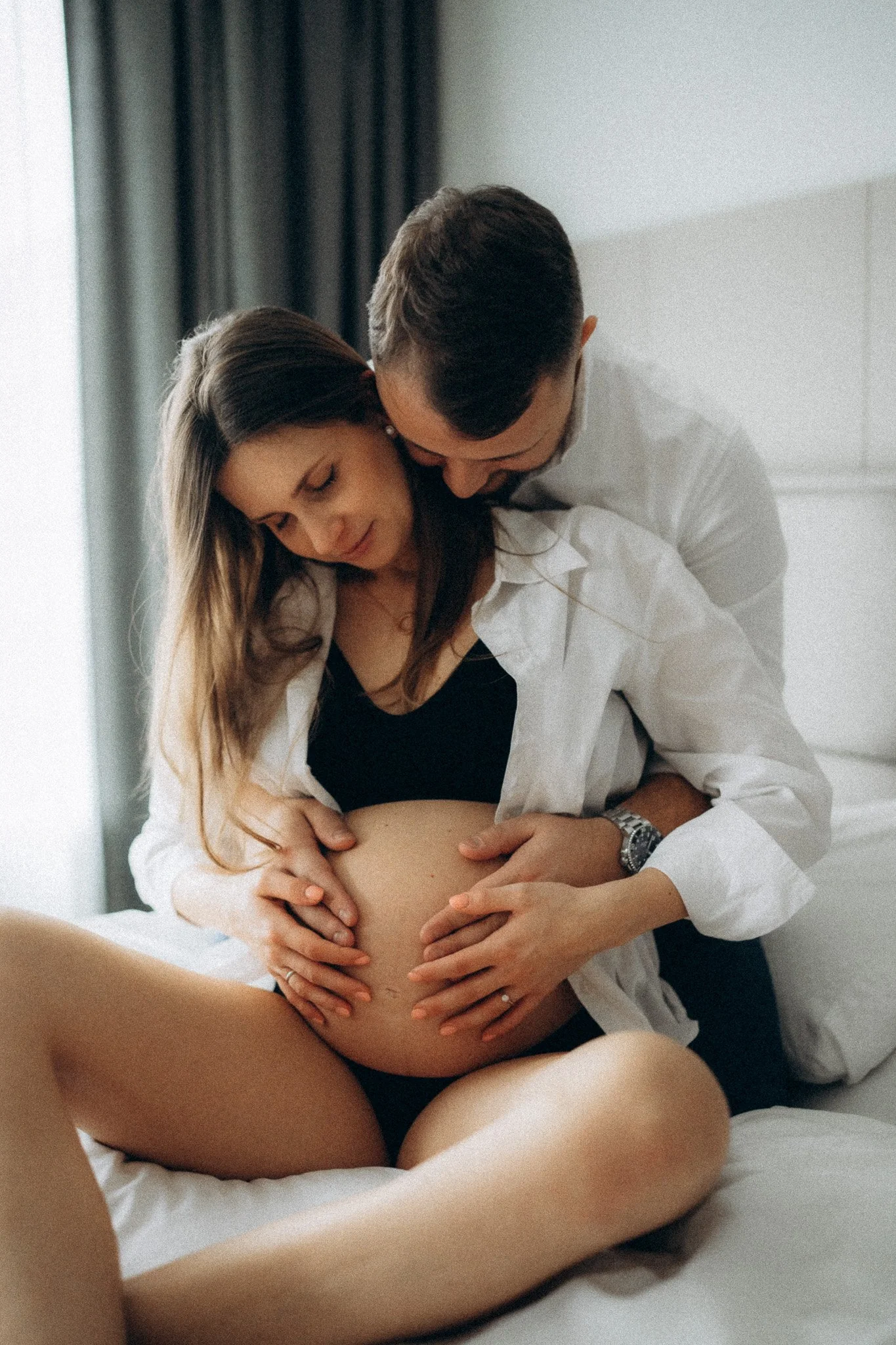 Partner objímá těhotnou ženu a těhotenské bříško během domácího focení