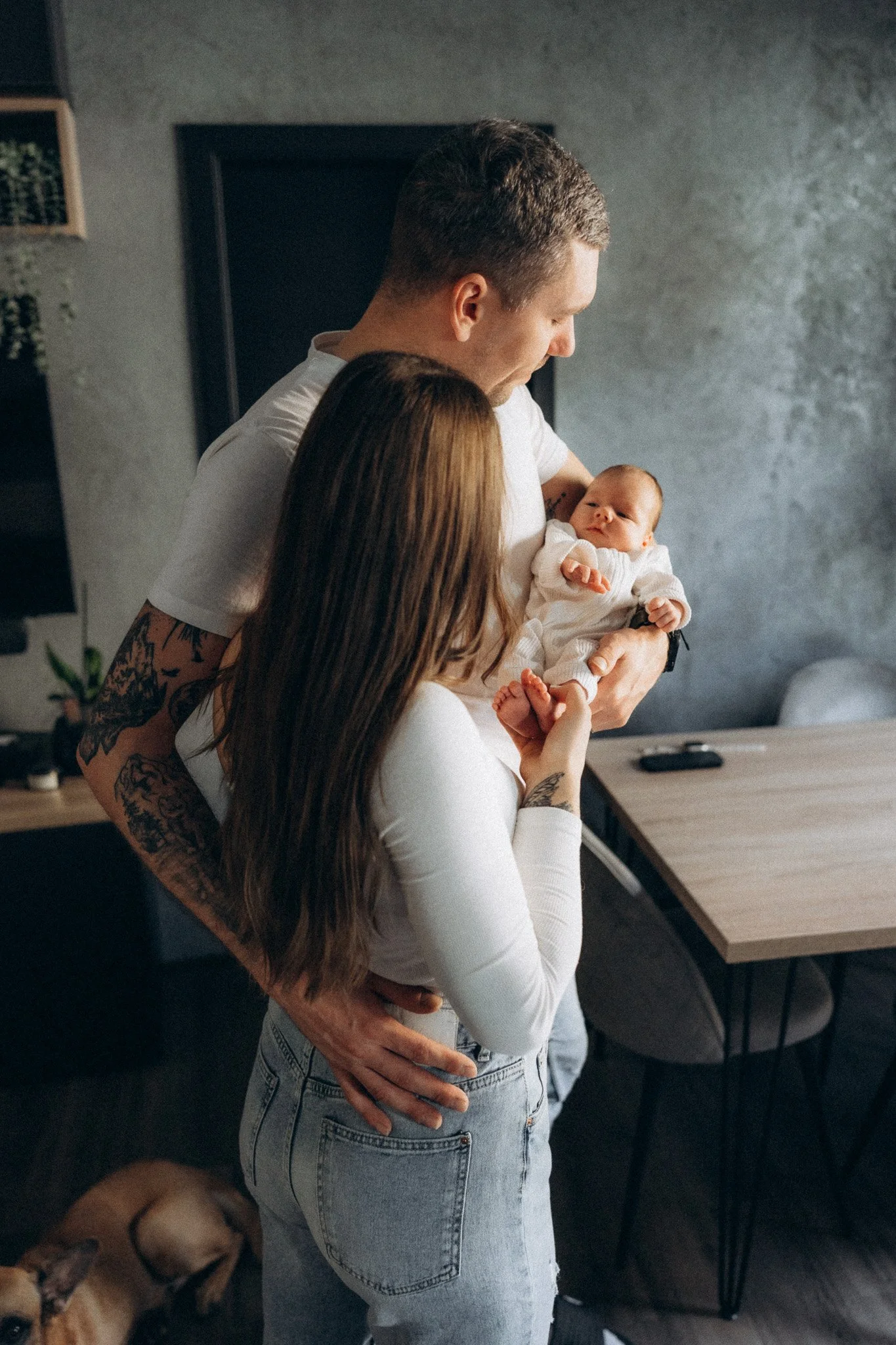 Tatínek objímá maminku a společně hledí na novorozené miminko