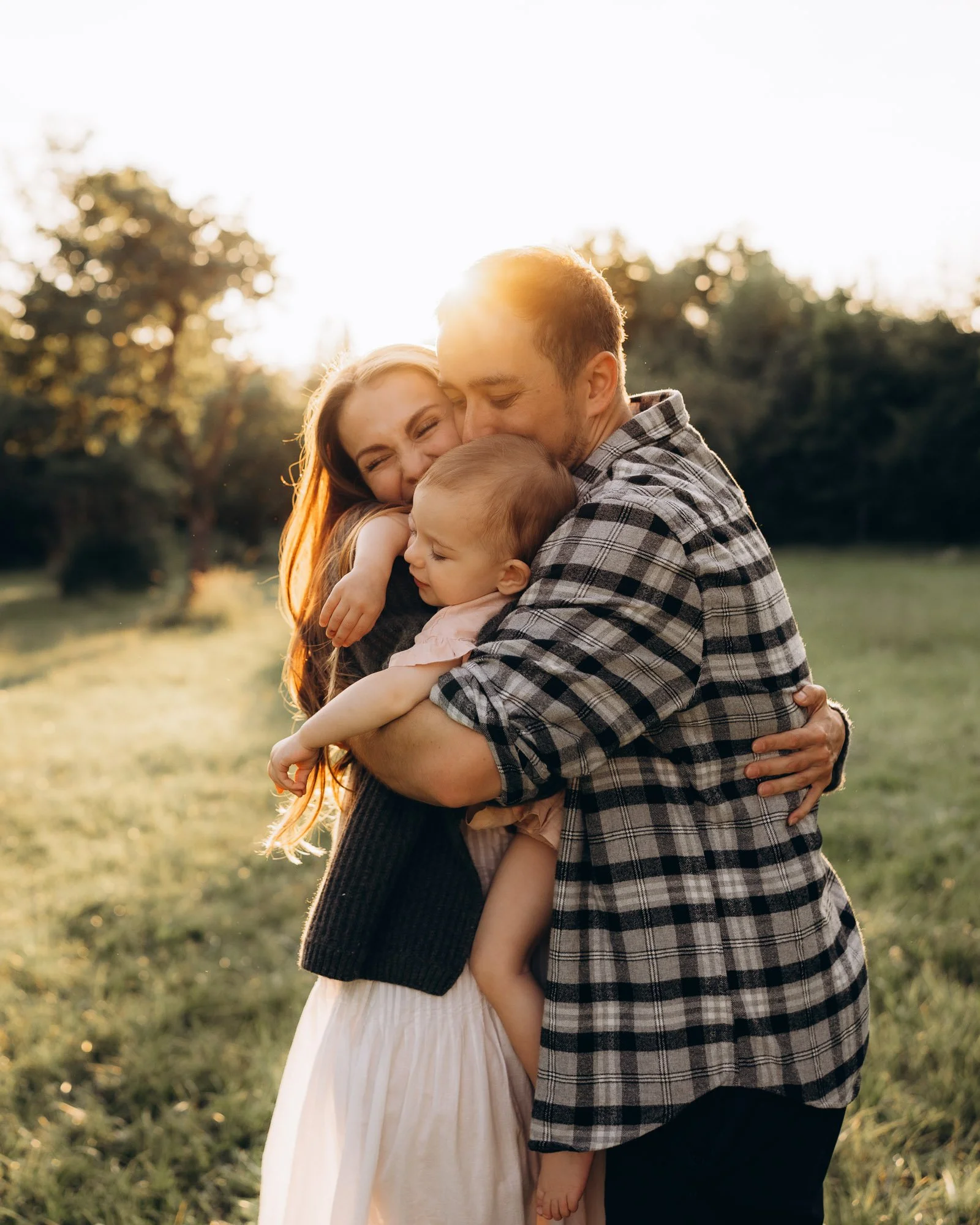 Rodinné focení v přírodě při západu slunce - intimní moment rodičů s dítětem v náručí.