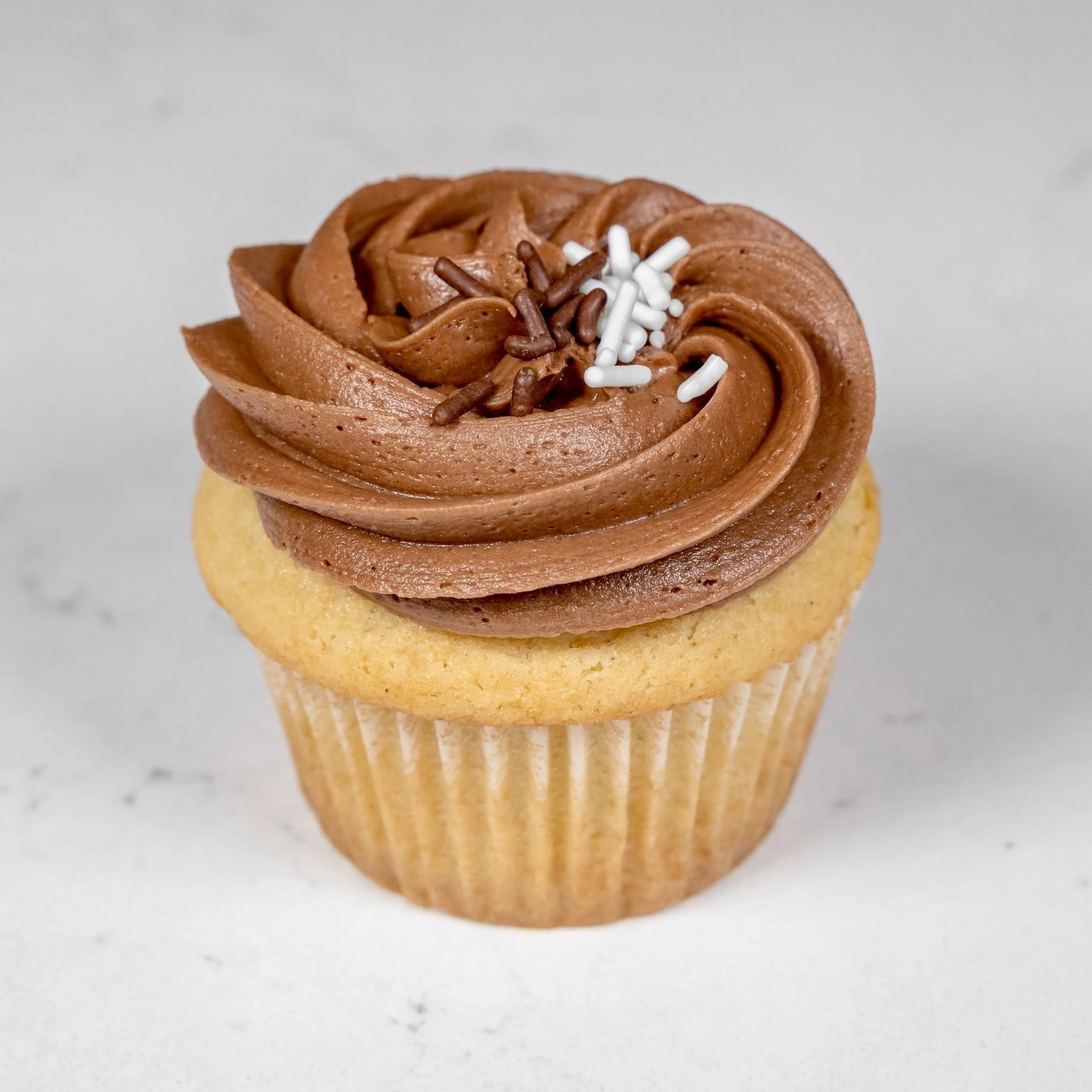 Vanilla cupcake with chocolate frosting and sprinkles on a marble surface.