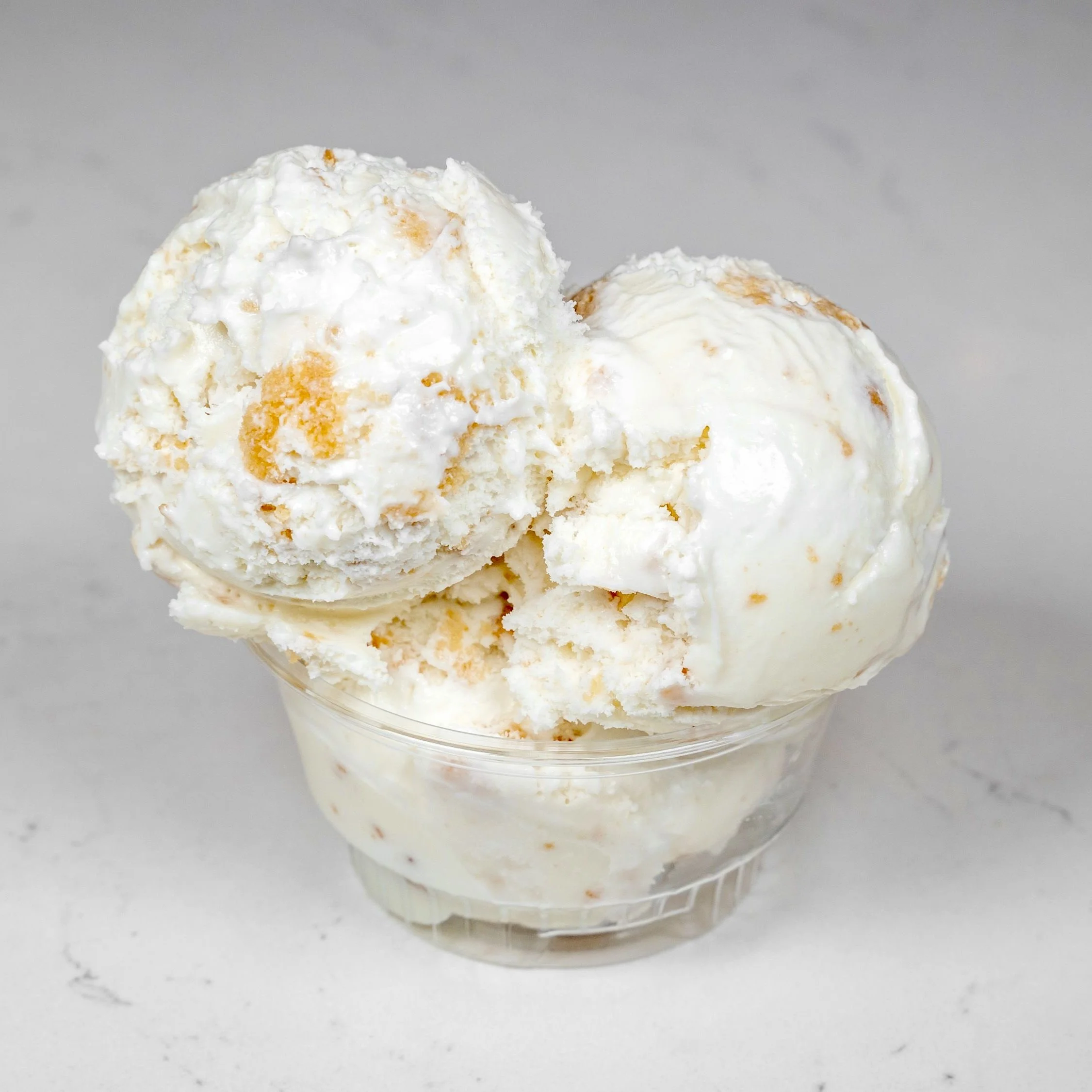 Vanilla ice cream with chunks in a plastic cup on a white surface.