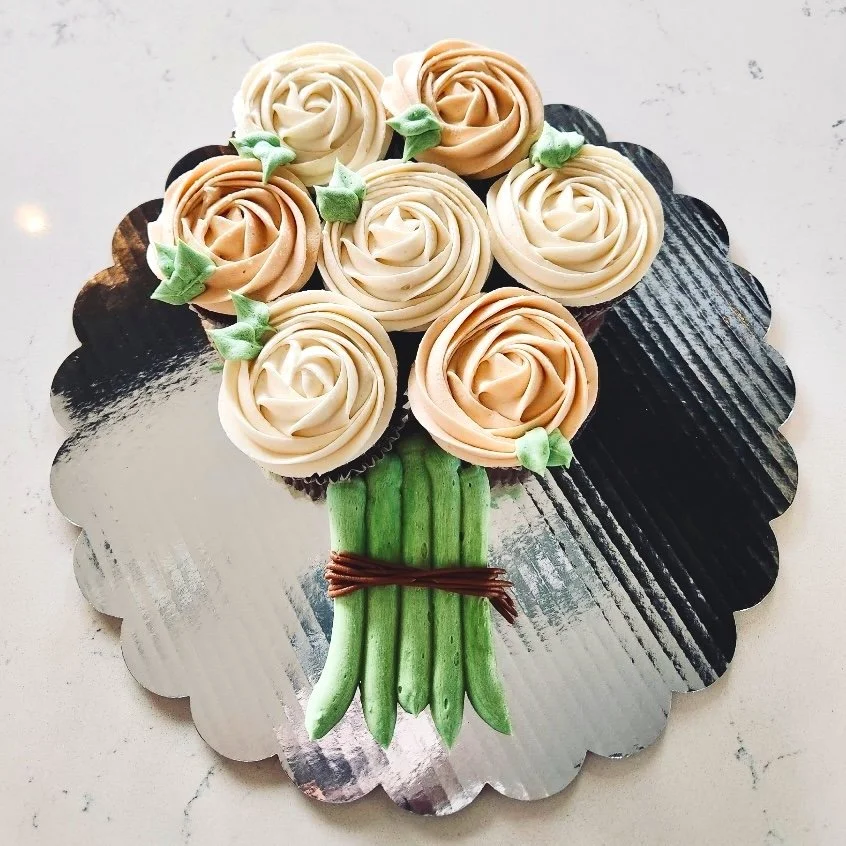 Cupcakes arranged to resemble a flower bouquet, with rose-shaped frosting and green fondant stems on a cakeboard