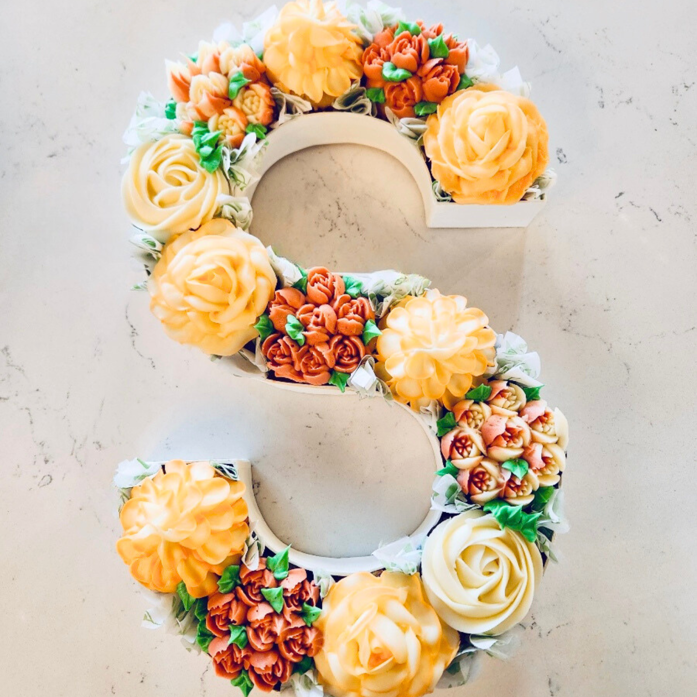 Letter S with floral decorated cupcakes.