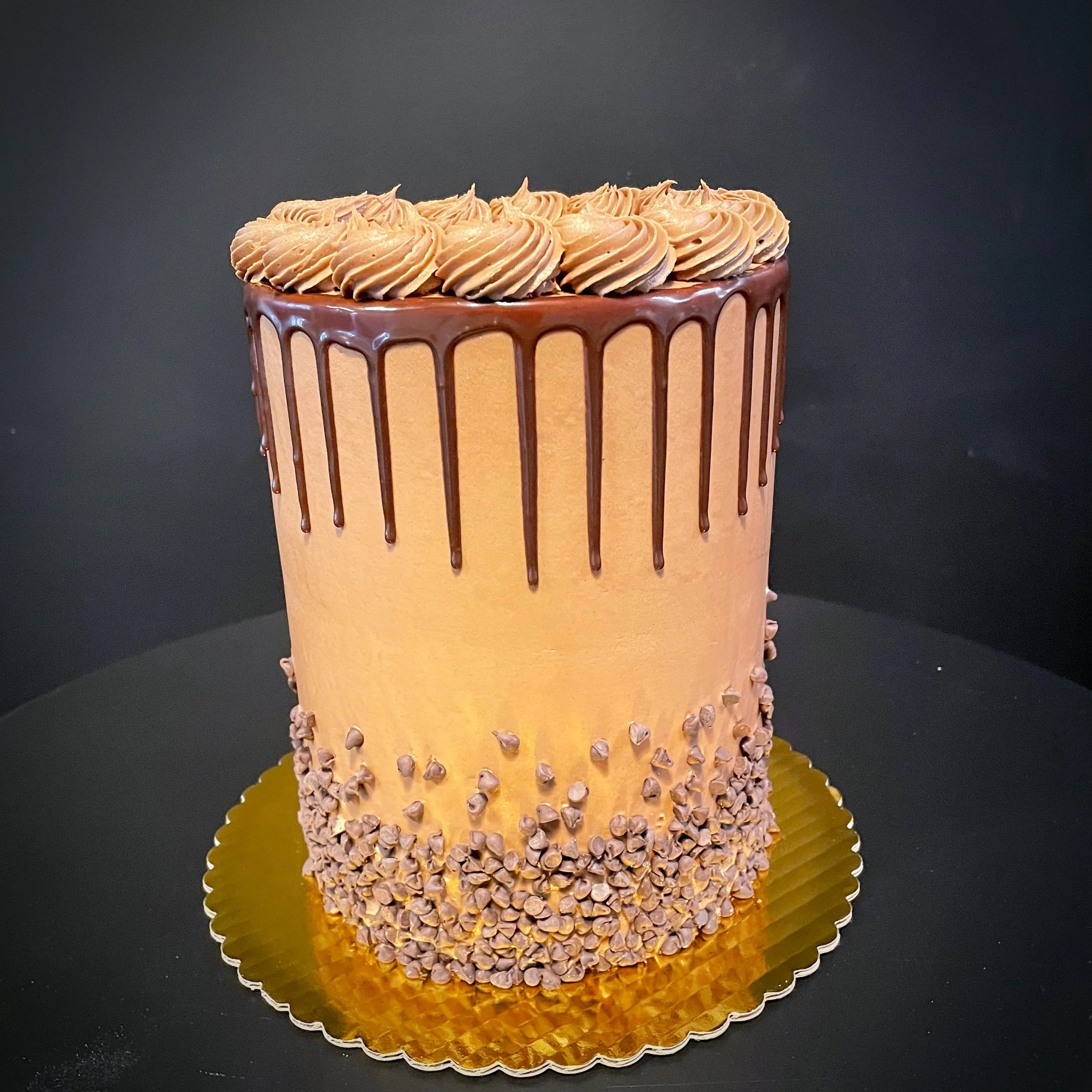 Chocolate drip cake with swirled frosting and chocolate chips on a gold base.