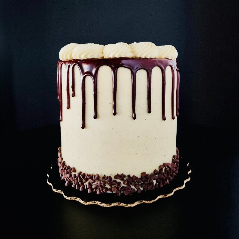 Tall cake with vanilla frosting, chocolate drip, and chocolate chips at the base.