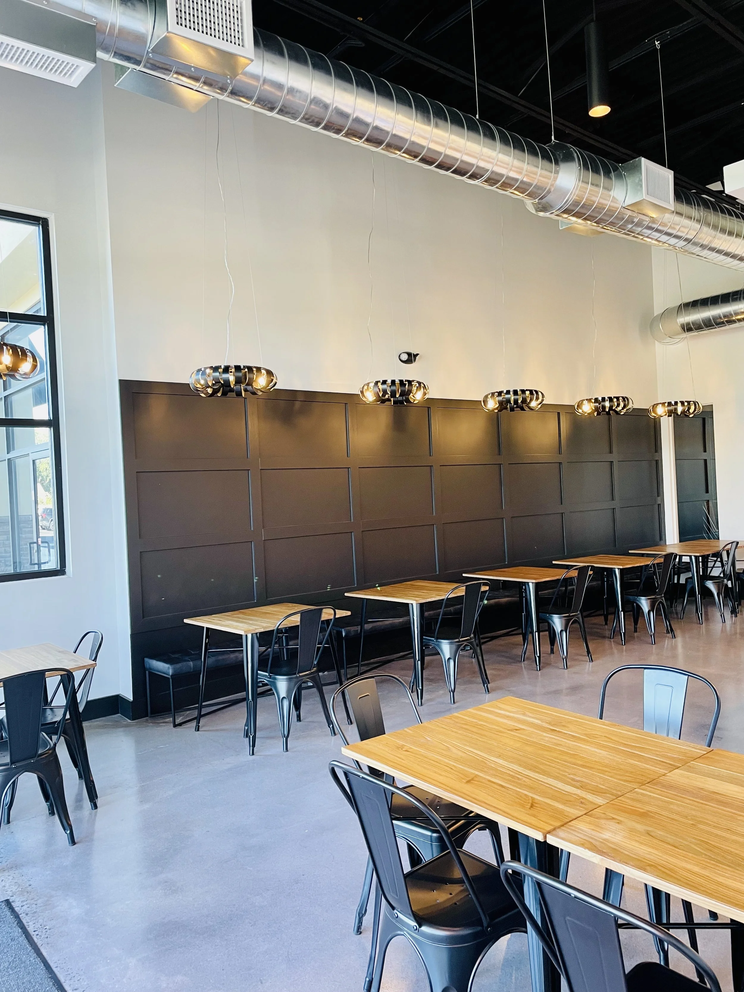 Interior of SUGARED with wooden tables, black metal chairs, industrial lighting, and exposed ceiling.