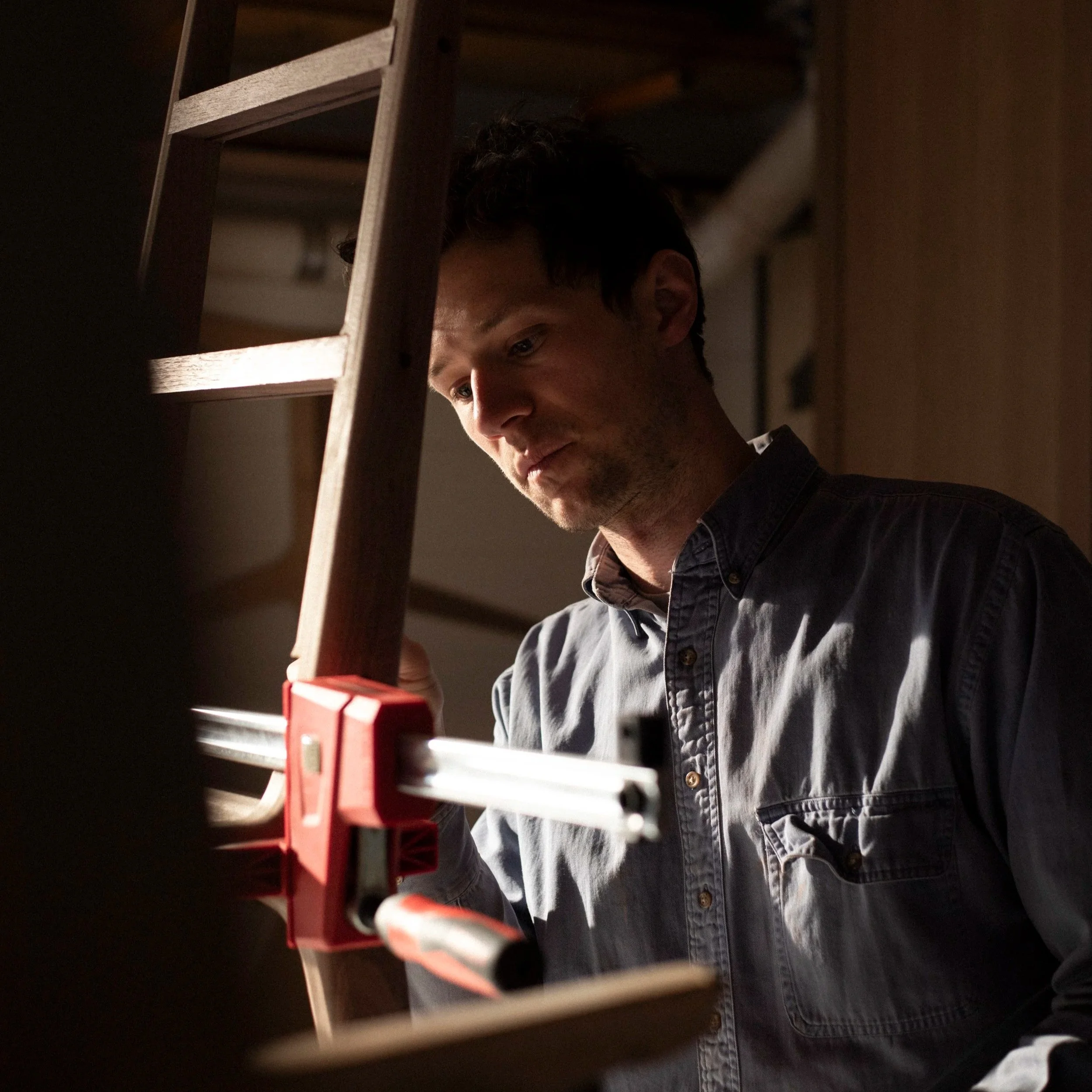 craftsperson inspects the quality of a walnut highback chair glue-up in a warmly lit shop space