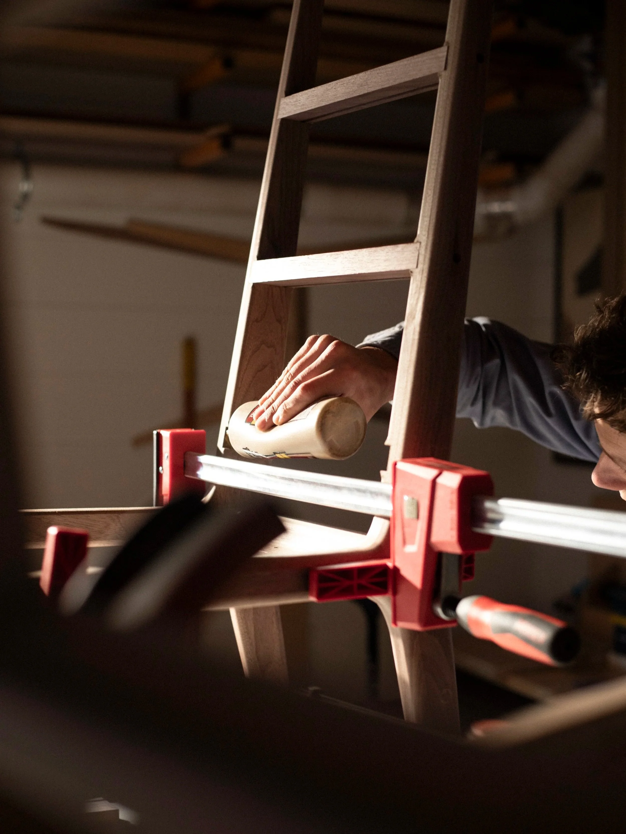 craftsman applying glue for final assembly of a walnut dining chair in a warmly lit shop space