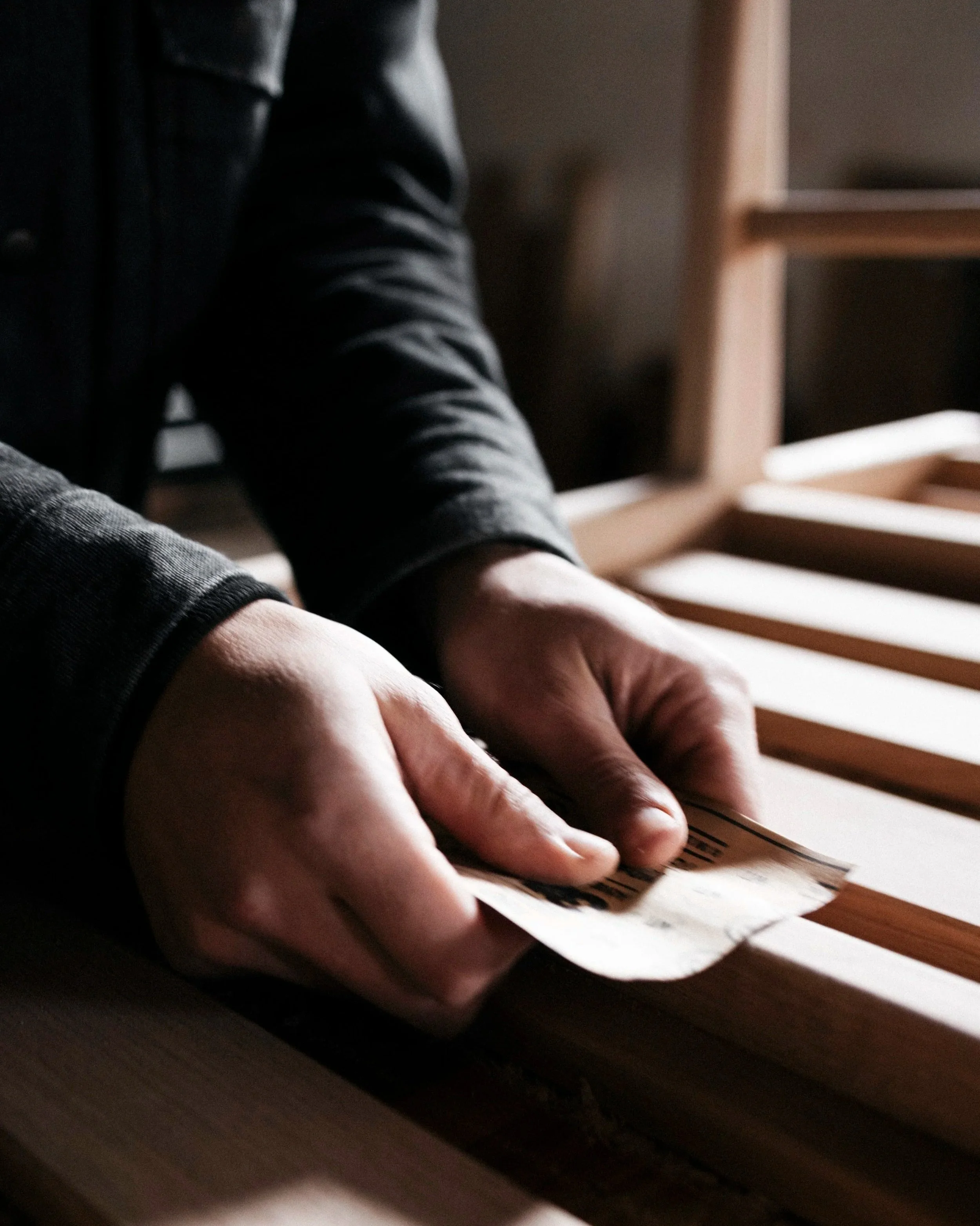 seasoned hands sand a piece of white oak furniture smooth in an industrial, dusty shop setting