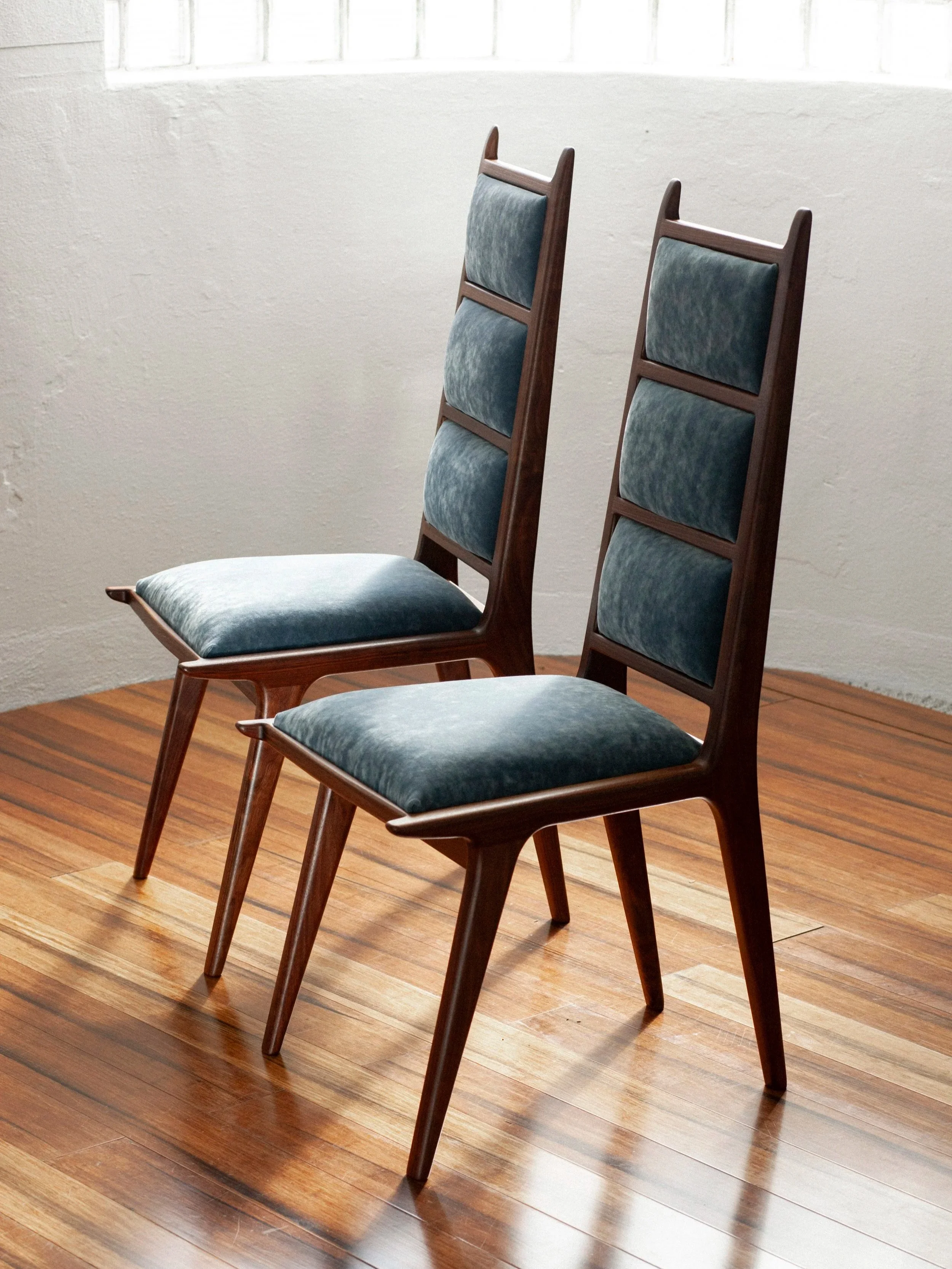 two walnut high back dining chairs sit side by side in a naturally lit studio setting