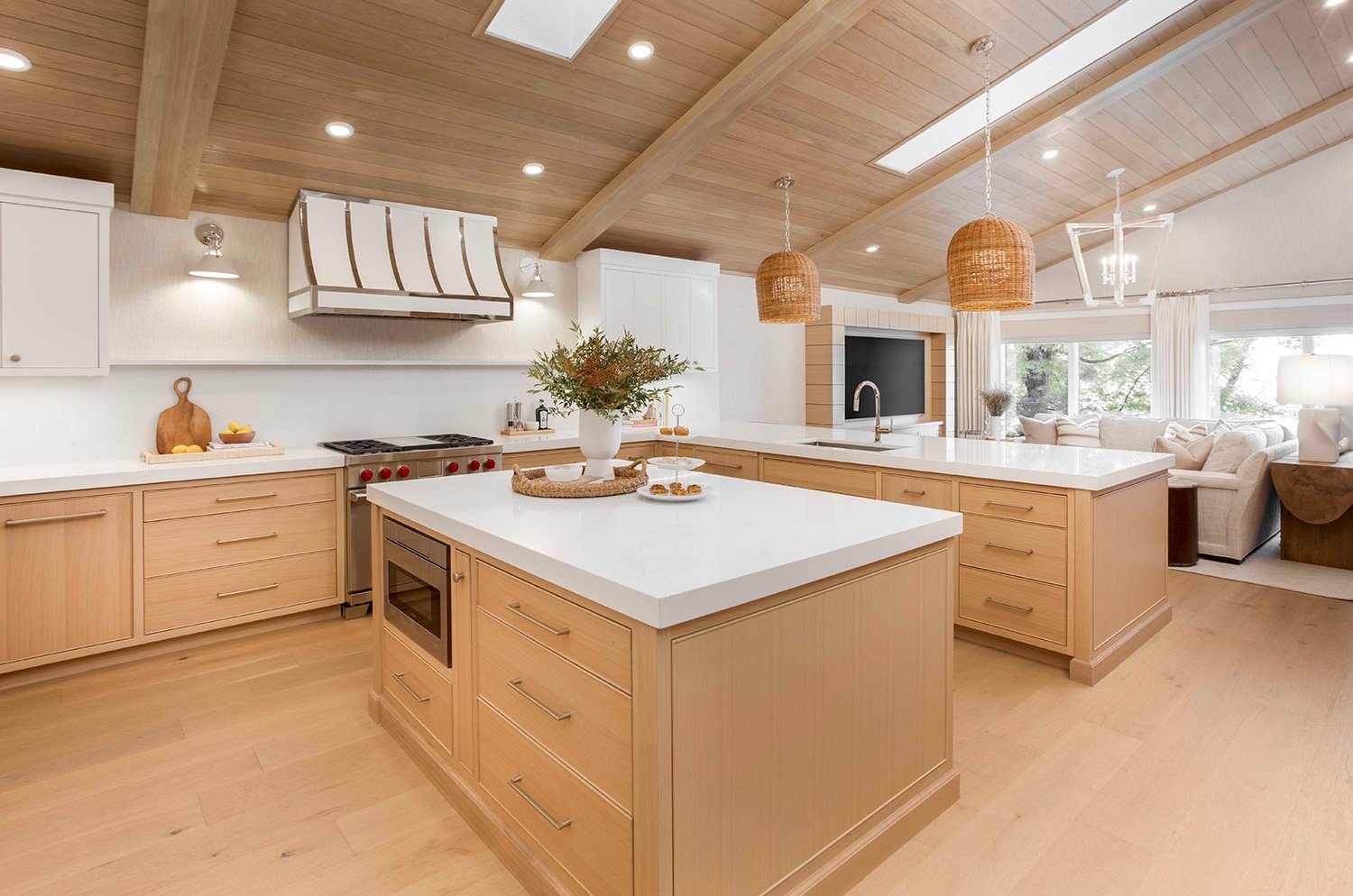 Bright lakehouse kitchen with natural white oak cabinetry, a large center island, woven pendant lighting, and light-filled surfaces that reflect a calm, serene palette | Ducy Design