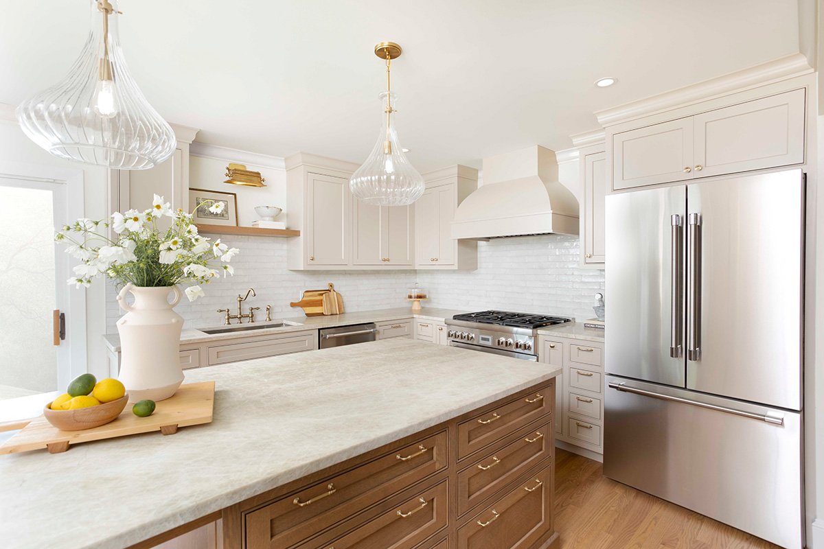 Bright transitional kitchen with white cabinetry, a warm wood island, brass hardware, glass pendant lights, and a custom range hood in a Ducy Design residential project