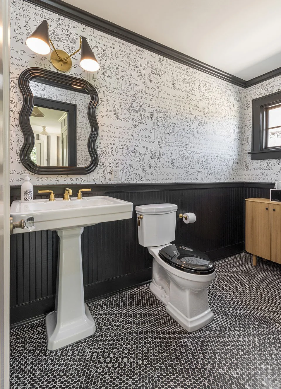 Bold powder bath with a decorative framed mirror, black painted walls, mosaic penny tile floor, pedestal sink, and gold fixtures | Ducy Design