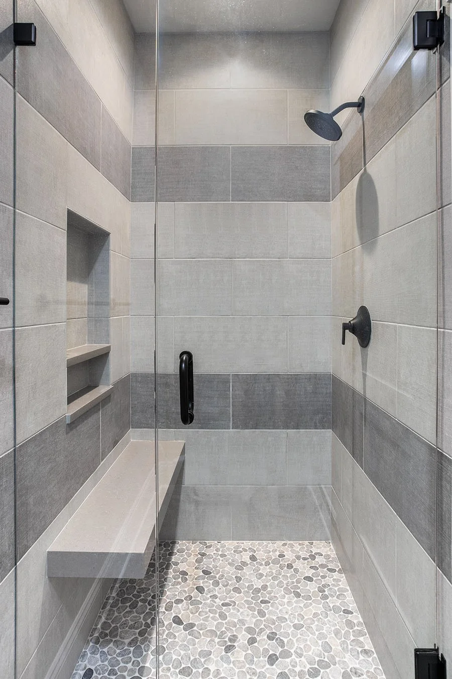 Cleveland Ohio shower with large format gray wall tile and pebble floor tile black shower hinges quartz floating shower bench