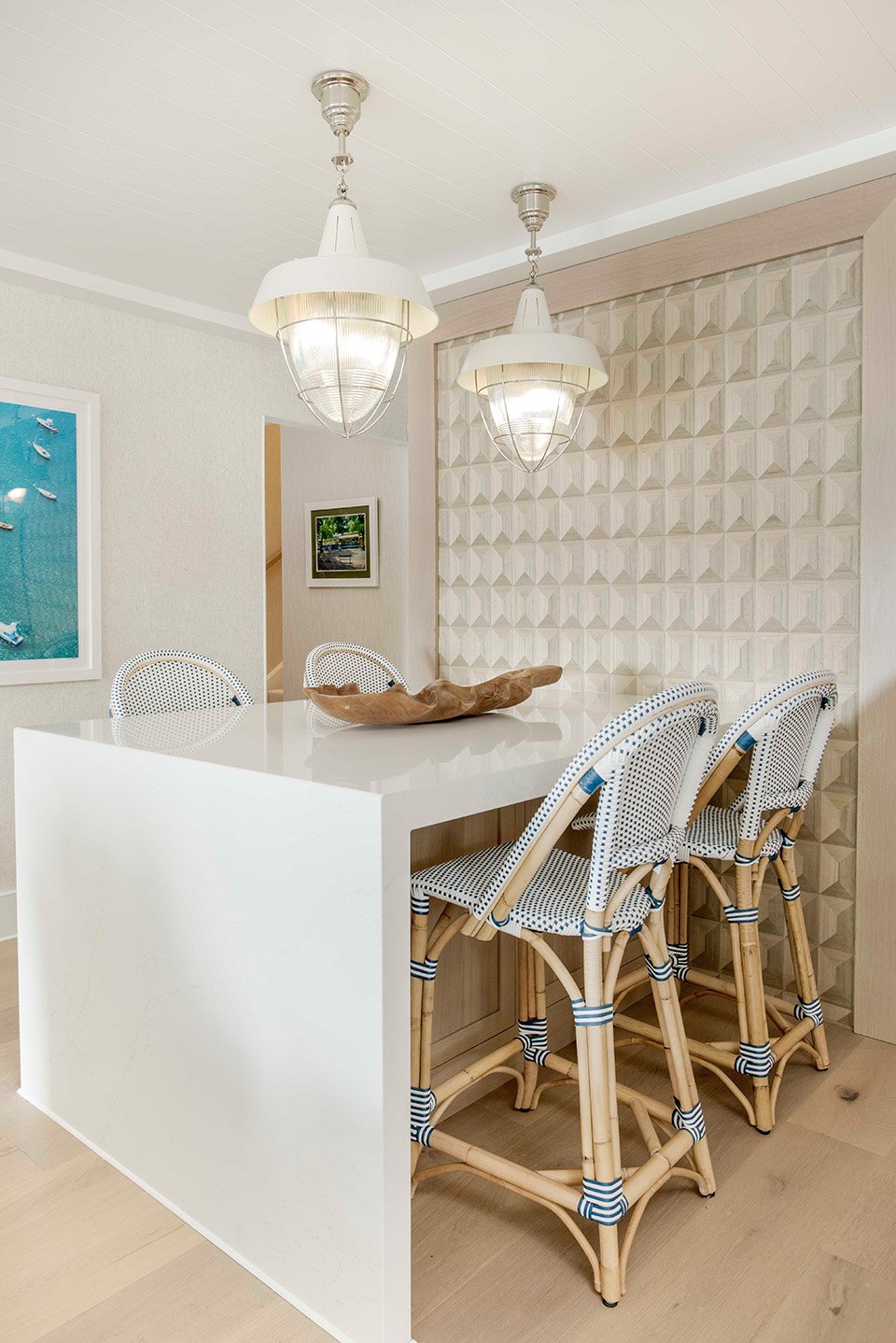 Alternate angle of the lakehouse kitchen and dining area with woven pendant lighting, white bar stools, and warm wood cabinetry bathed in natural light | Ducy Design