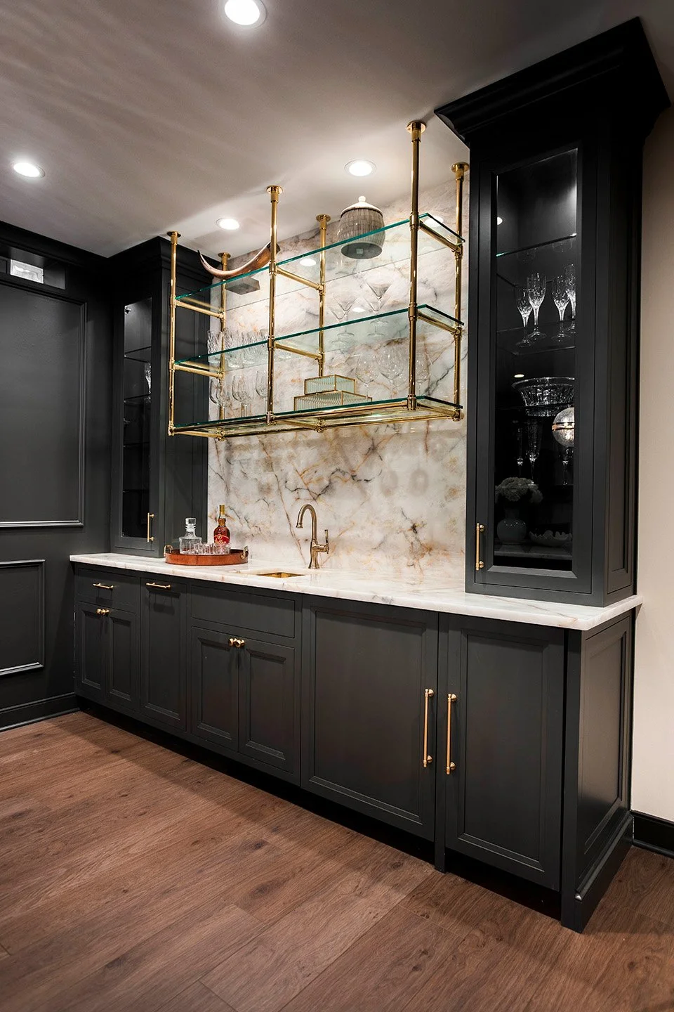 Dark bar cabinetry with glass-front display shelving, interior lighting, and refined hardware in the Luxe Lounge lower level | Ducy Design