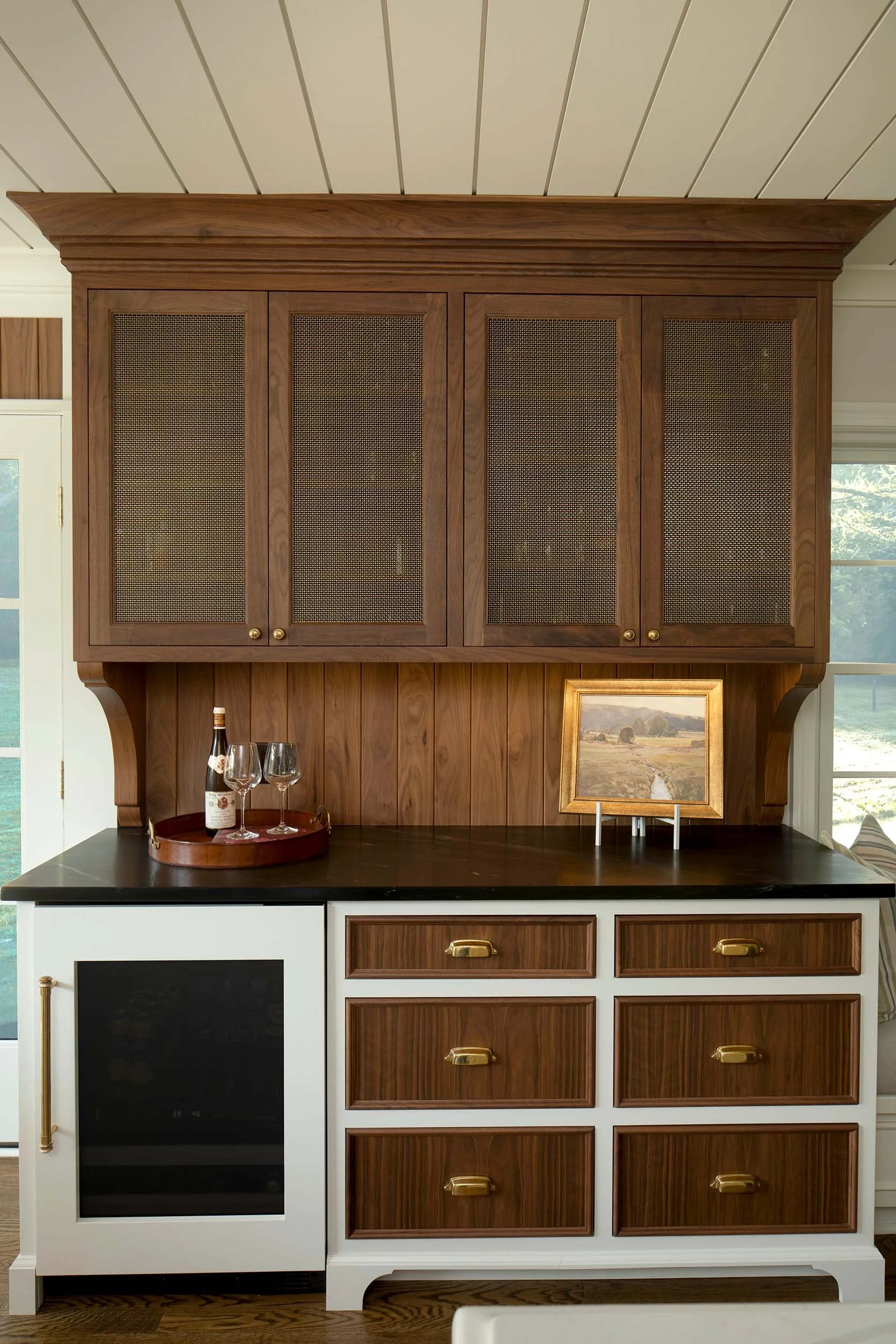 Custom walnut and white kitchen cabinetry with woven cabinet fronts, black countertop, and antique brass hardware