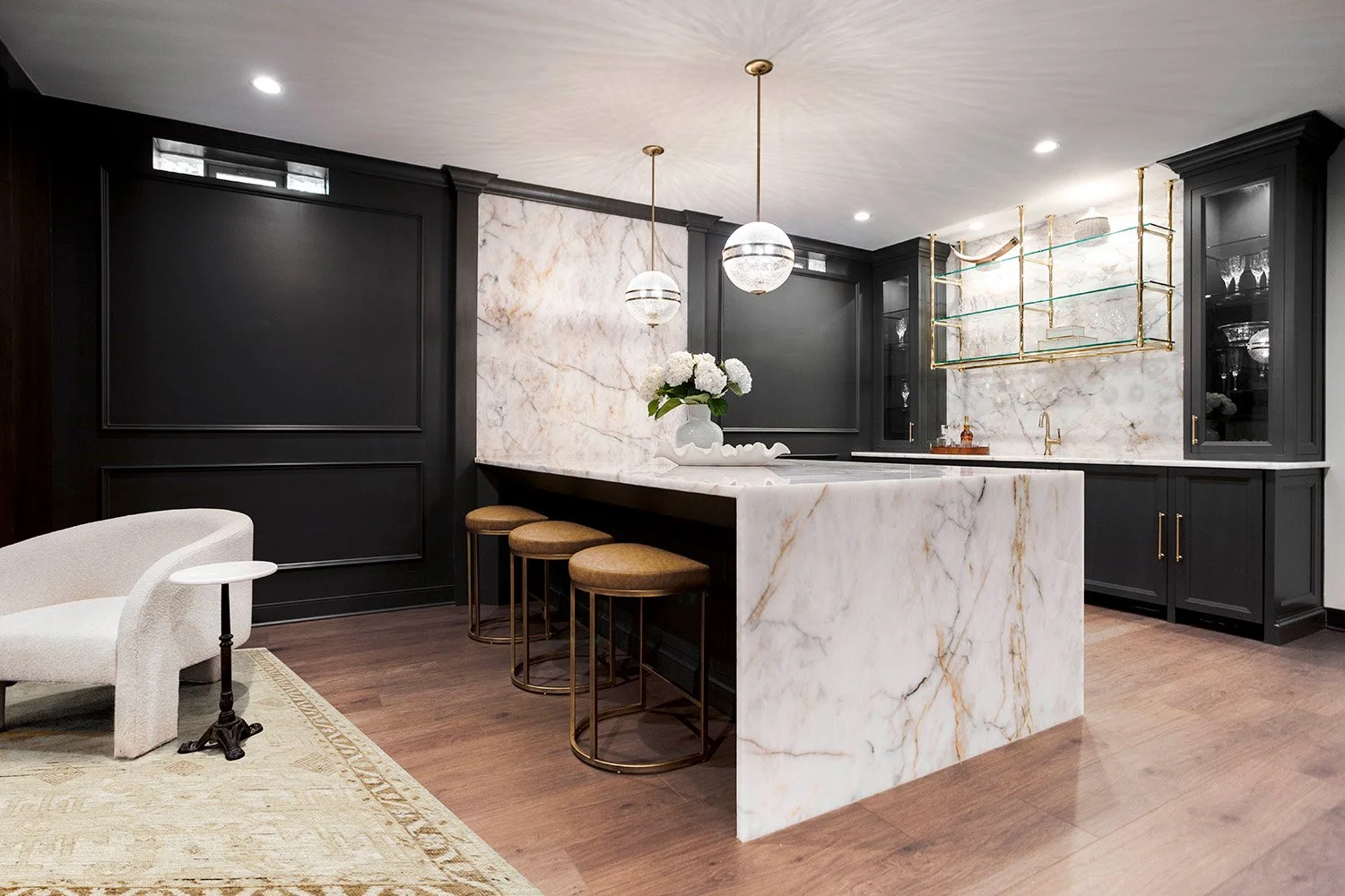 Custom bar with dark painted cabinetry, a Crystal Thunder quartzite countertop, open glass shelving, and warm accent lighting | Ducy Design