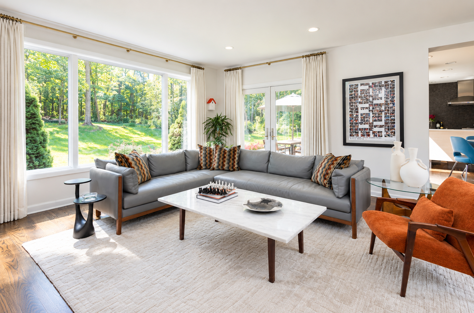 Mid-century modern family room featuring a gray sectional sofa, orange accent chairs, marble coffee table, and expansive windows with custom drapery.