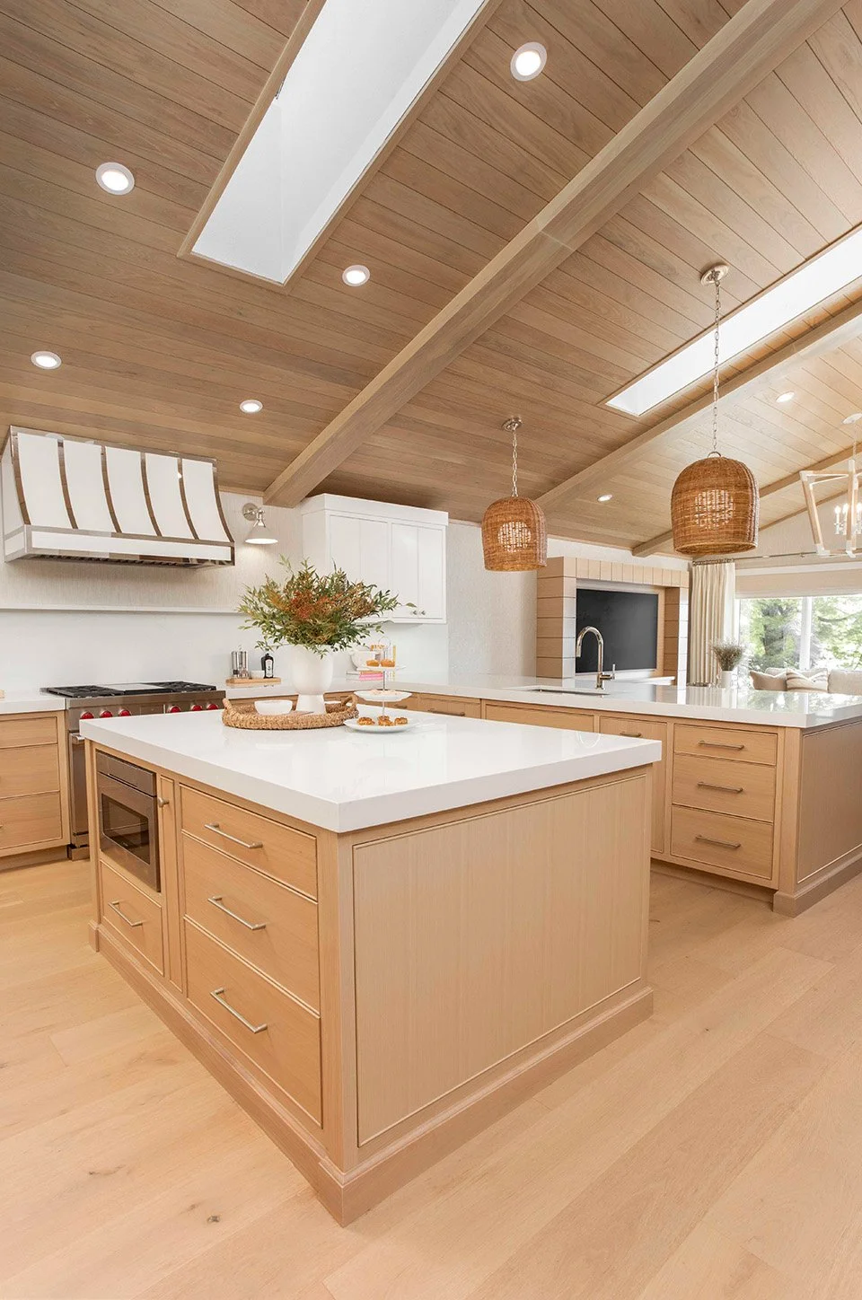 Wide shot of the lakehouse kitchen featuring a two-tone nickel and white range hood, natural wood cabinetry, a large island, and bright airy finishes | Ducy Design