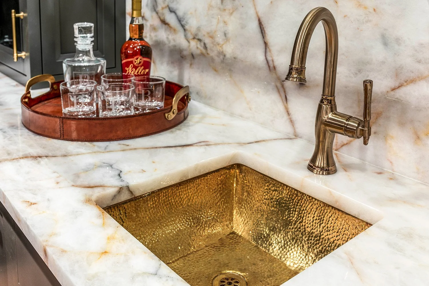 Detail of a hammered gold undermount bar sink set into a Crystal Thunder quartzite countertop with a brushed gold faucet | Ducy Design