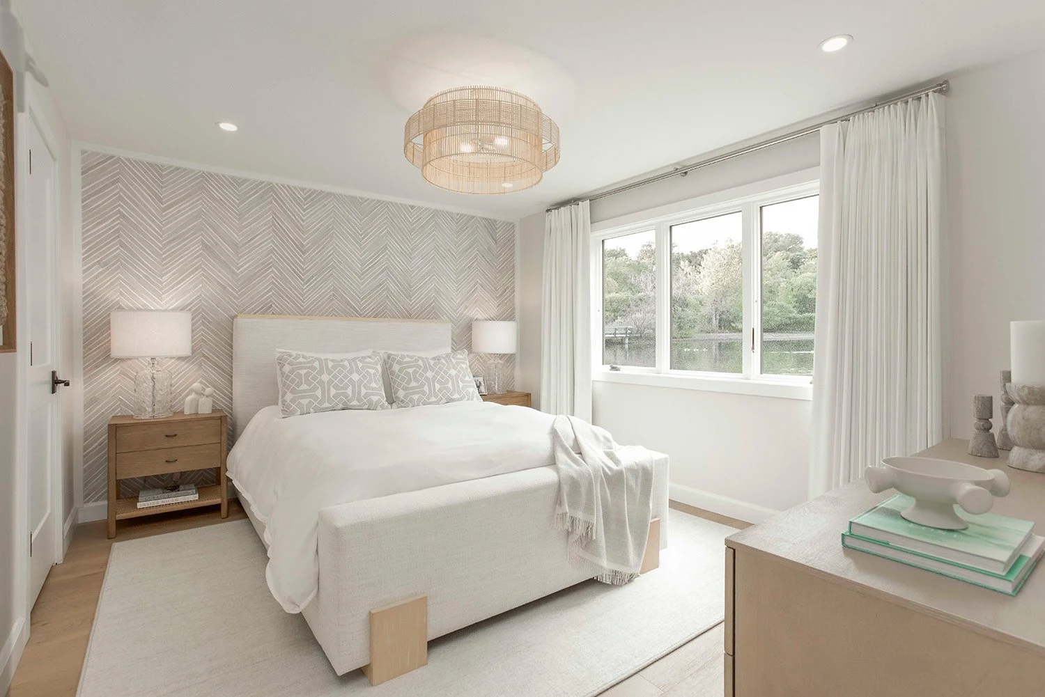 Calm primary bedroom with layered white and neutral bedding, a wood platform bed, soft natural light, and a serene lakehouse atmosphere | Ducy Design