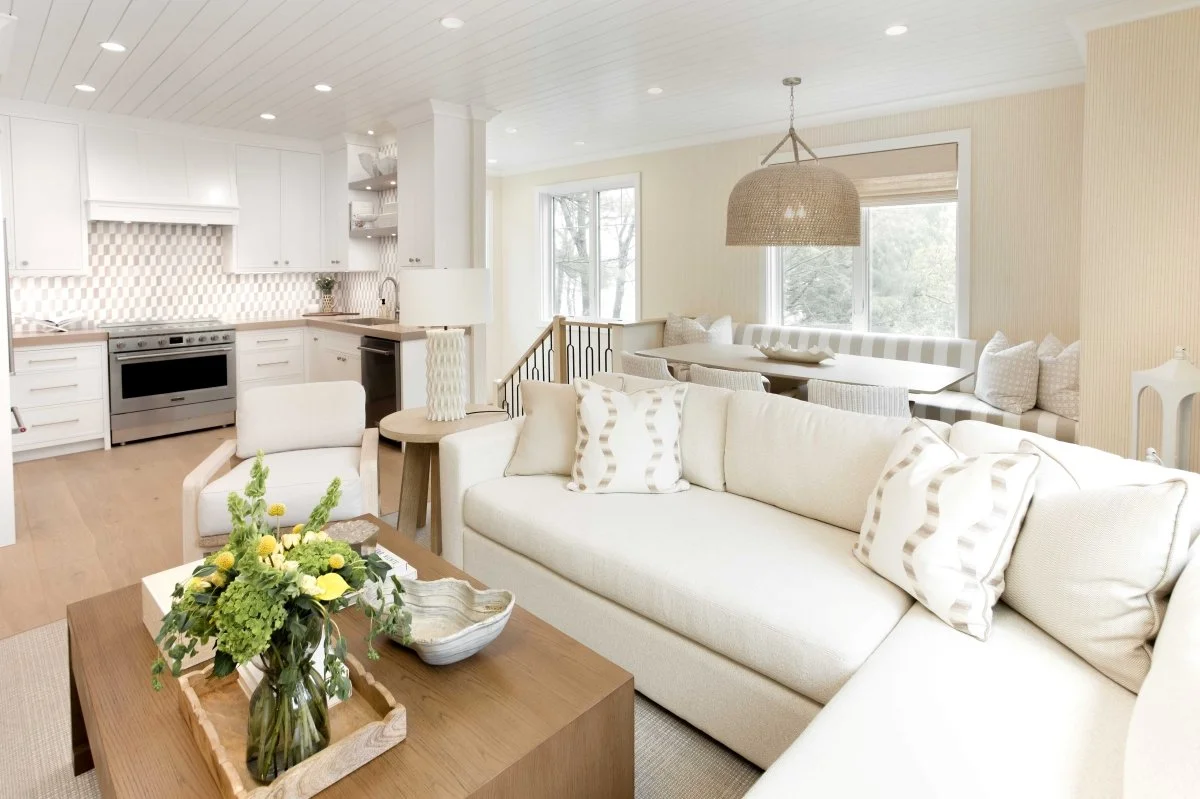 A neutral toned living area flows into a dining banquette and kitchen with a woven pendant light and checkered tile backsplash | Ducy Design