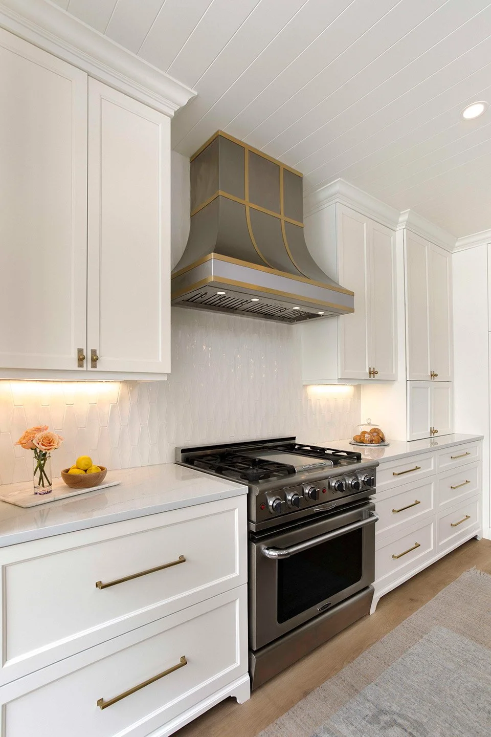 Detail view of a professional stainless steel range beneath a custom mixed-metal hood with gold accents in a luxury kitchen | Ducy Design