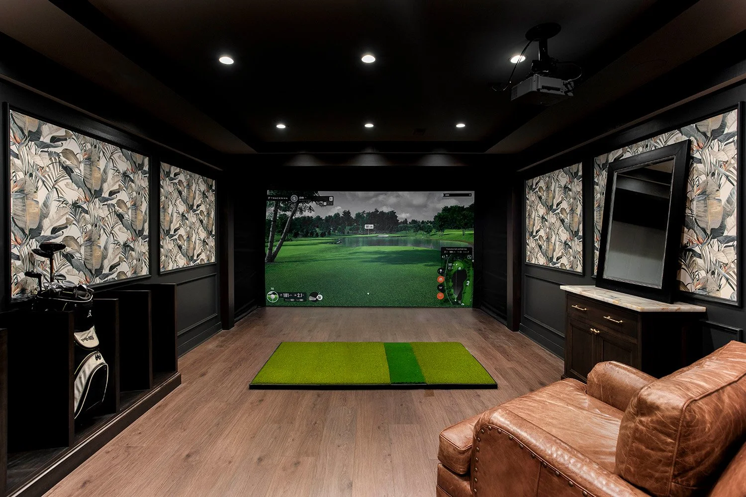 Lower level golf simulator room with warm wood accents, turf flooring, ambient lighting, and a large projection screen for an immersive experience | Ducy Design