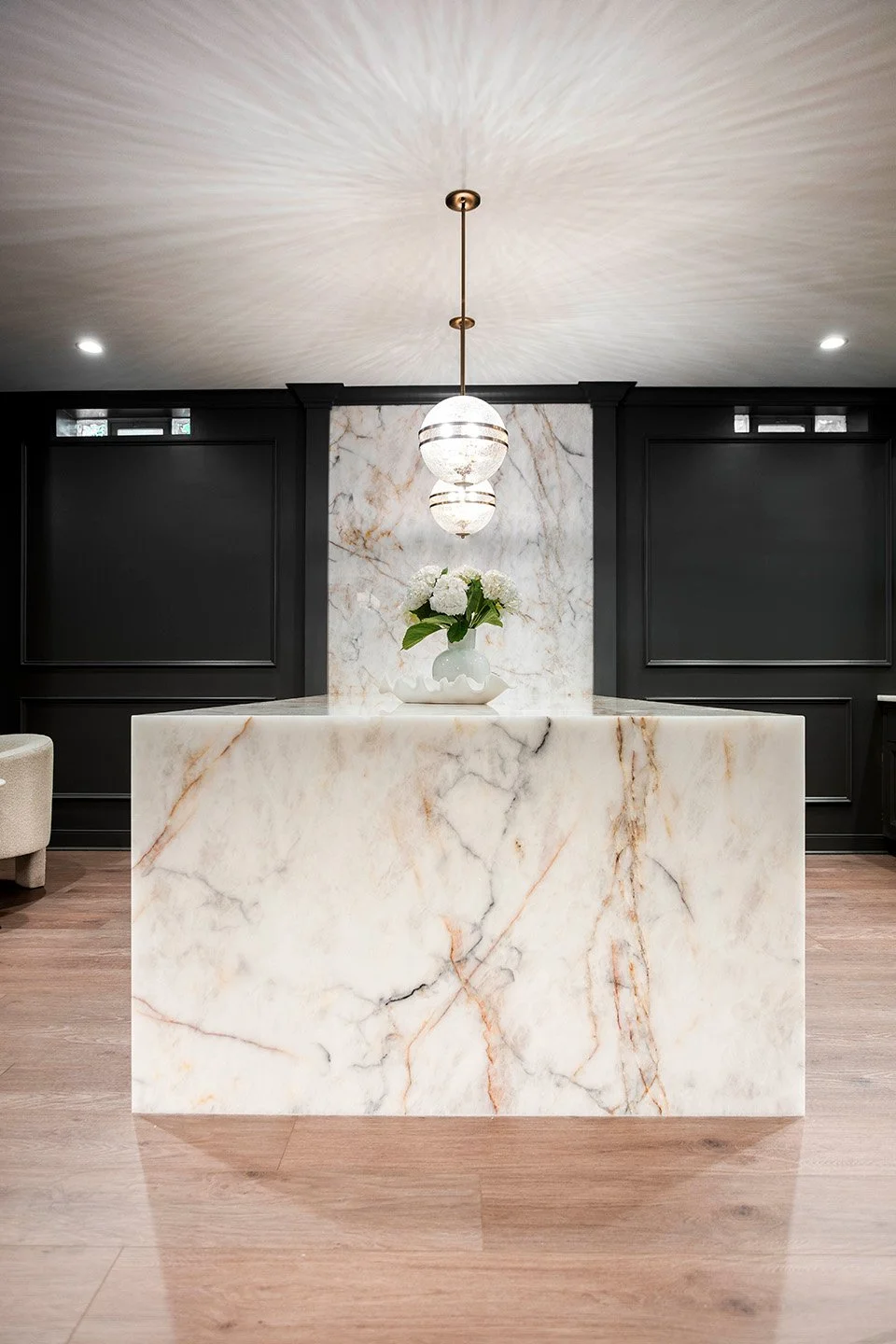 Bar area with a quartzite countertop, dark base cabinetry, a statement pendant light, and bar stool seating in a moody lower level lounge | Ducy Design