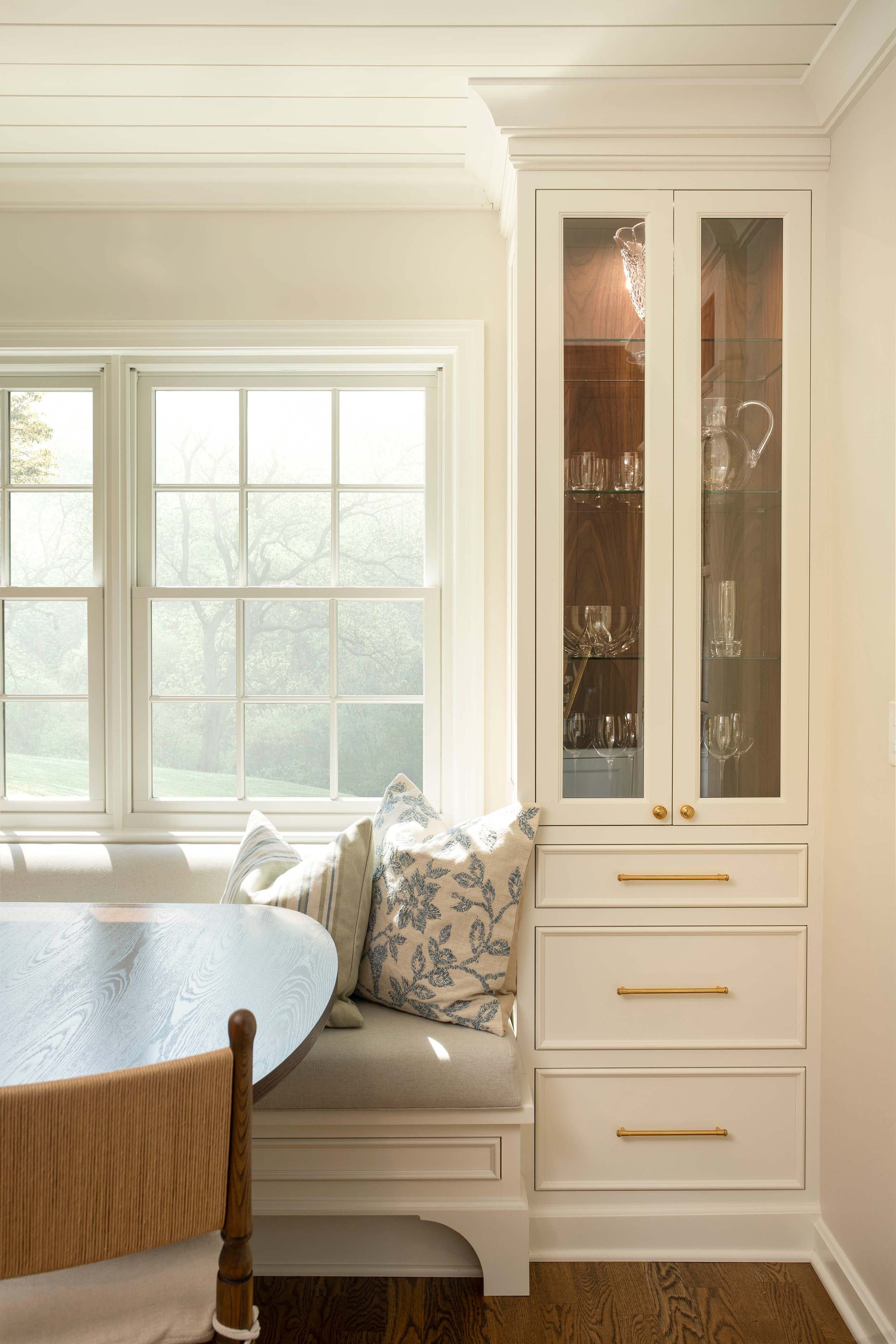 History Retold dining nook in Shaker Heights, Ohio with a custom built-in banquette, glass-front cabinetry, and floral pillows